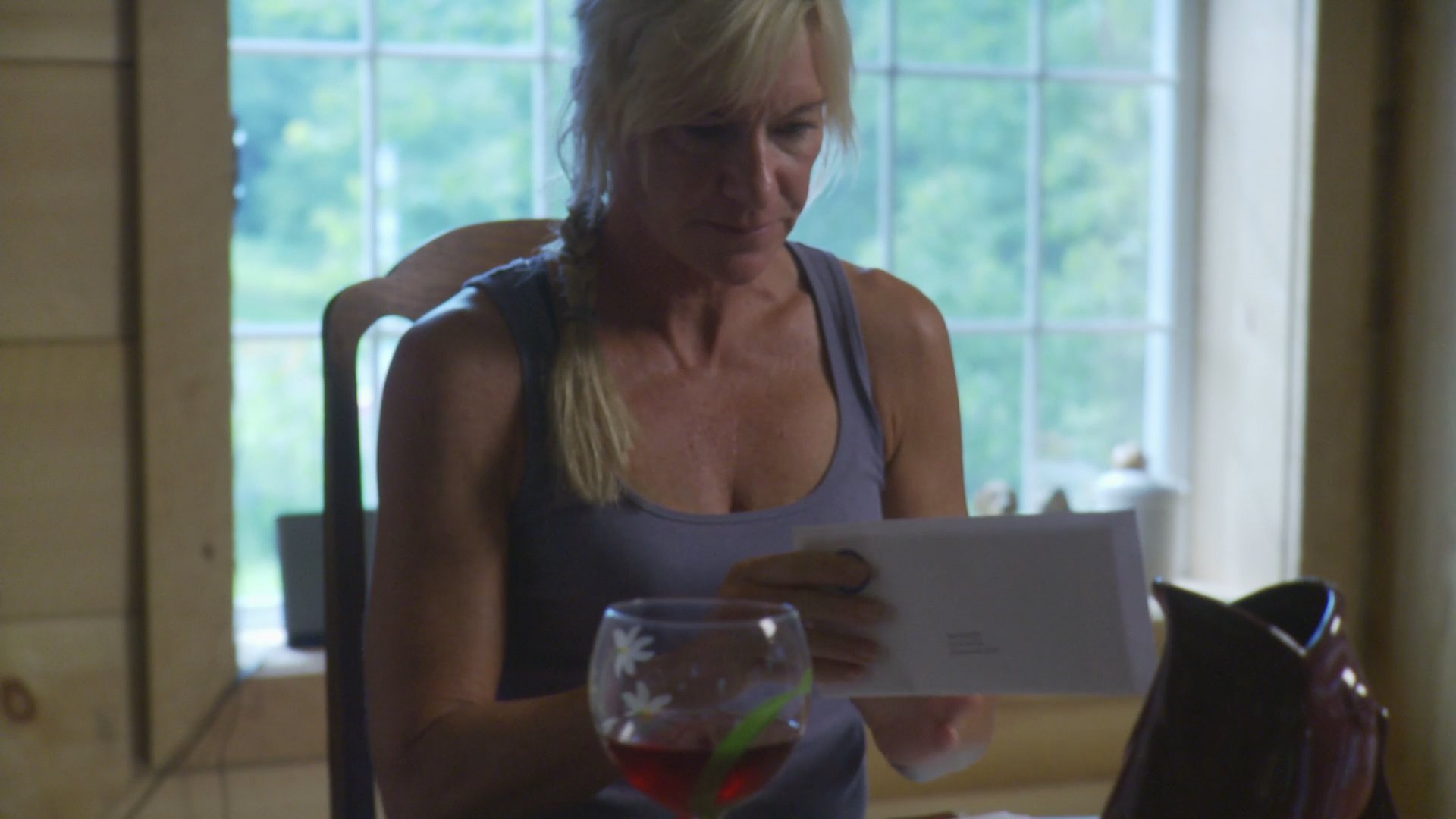 A woman sits at a table drinking wine while reviewing documents, accompanied by a golden retriever lying on the floor nearby.