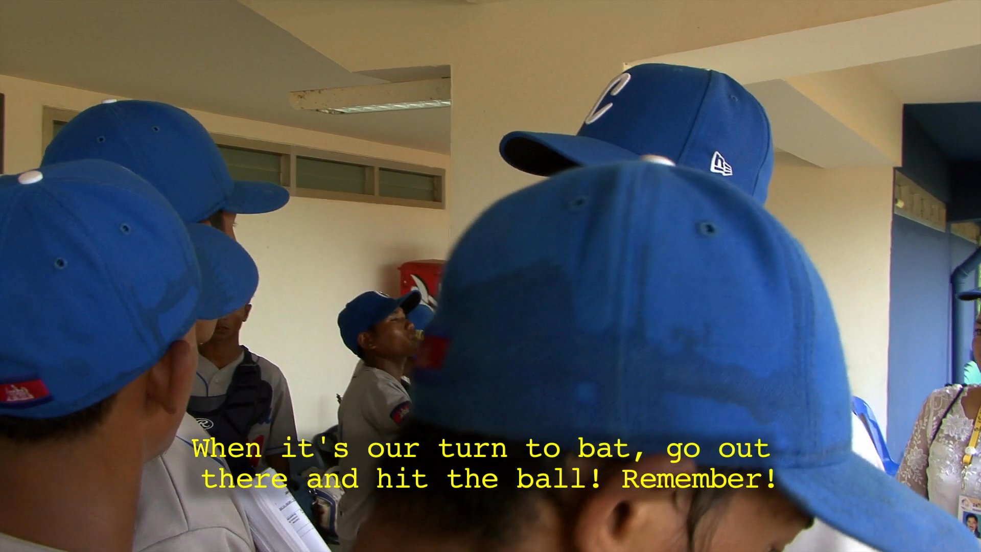 A baseball coach instructs his team in the dugout during a game against the Philippines, emphasizing technique and mindset to improve performance on the field.
