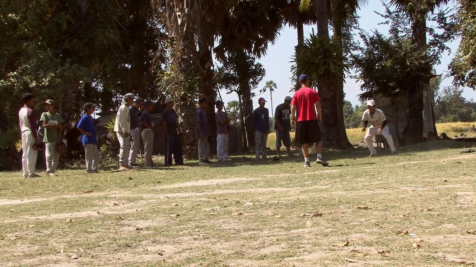 Young athletes engage in structured baseball defensive drills and physical conditioning exercises at an outdoor rural practice field.