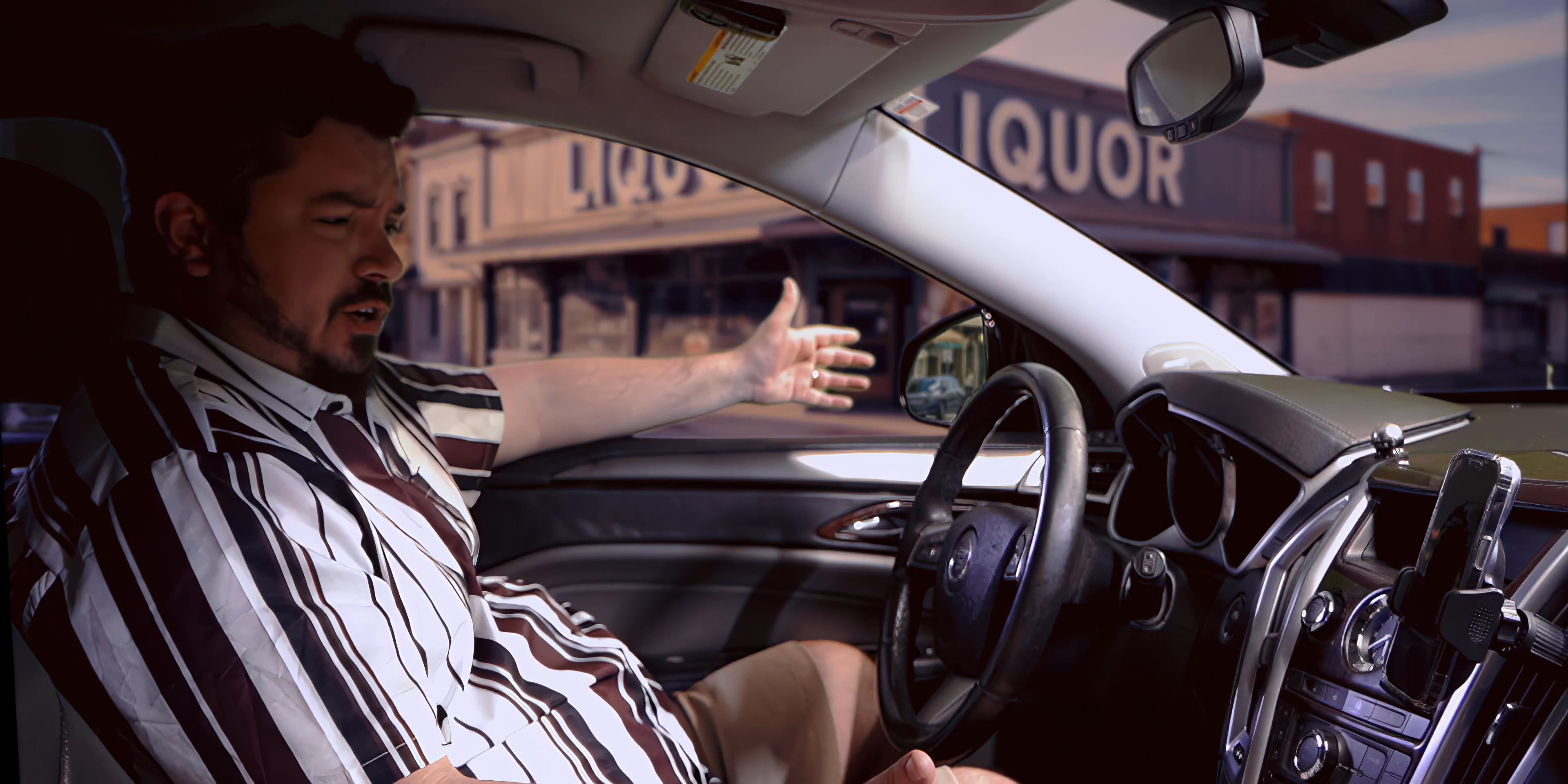 A man engaged in an active phone call while sitting in the driver seat of a parked vehicle. He gestures expressively during his conversation while an incoming call screen displays the contact name Kate.