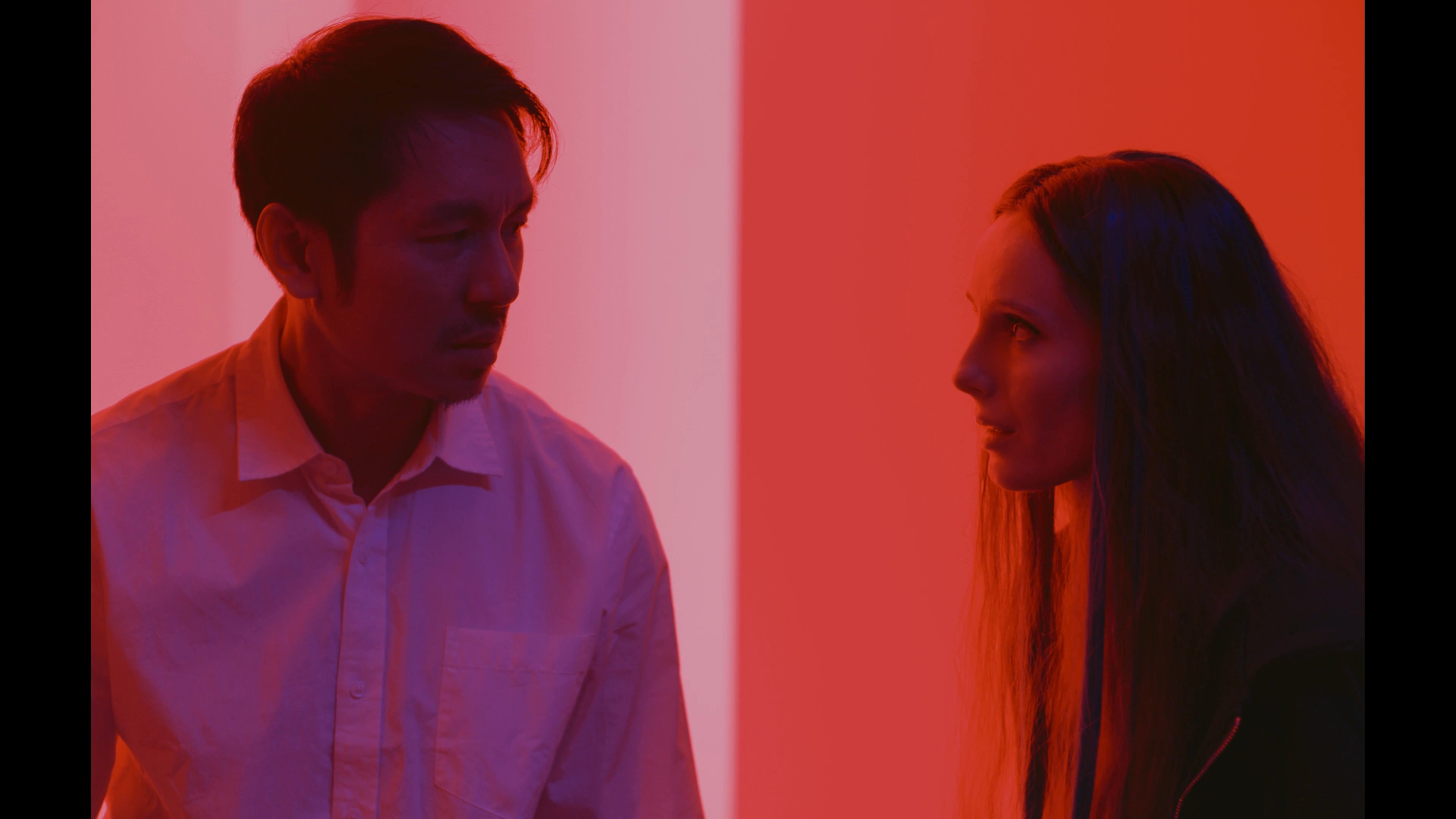 A woman with a blue wig and pearl necklace maintains a stoic demeanor, transitioning into an intense exchange between a man and a woman bathed in vibrant red lighting.