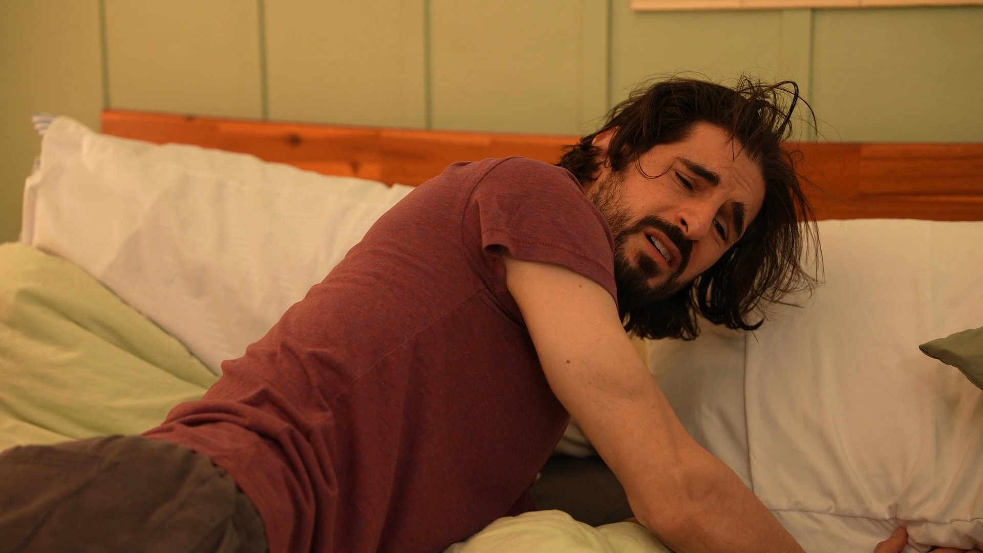 A woman provides professional support to a man experiencing emotional distress while he sits in a bedroom environment. She engages him in conversation, attempting to facilitate communication and provide comfort.