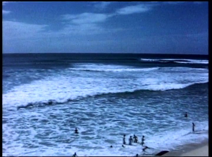 A powerful ocean swell breaks at a beach during a competitive surfing event. Contestants and a head judge gather on the sand for final instructions before the heat begins.