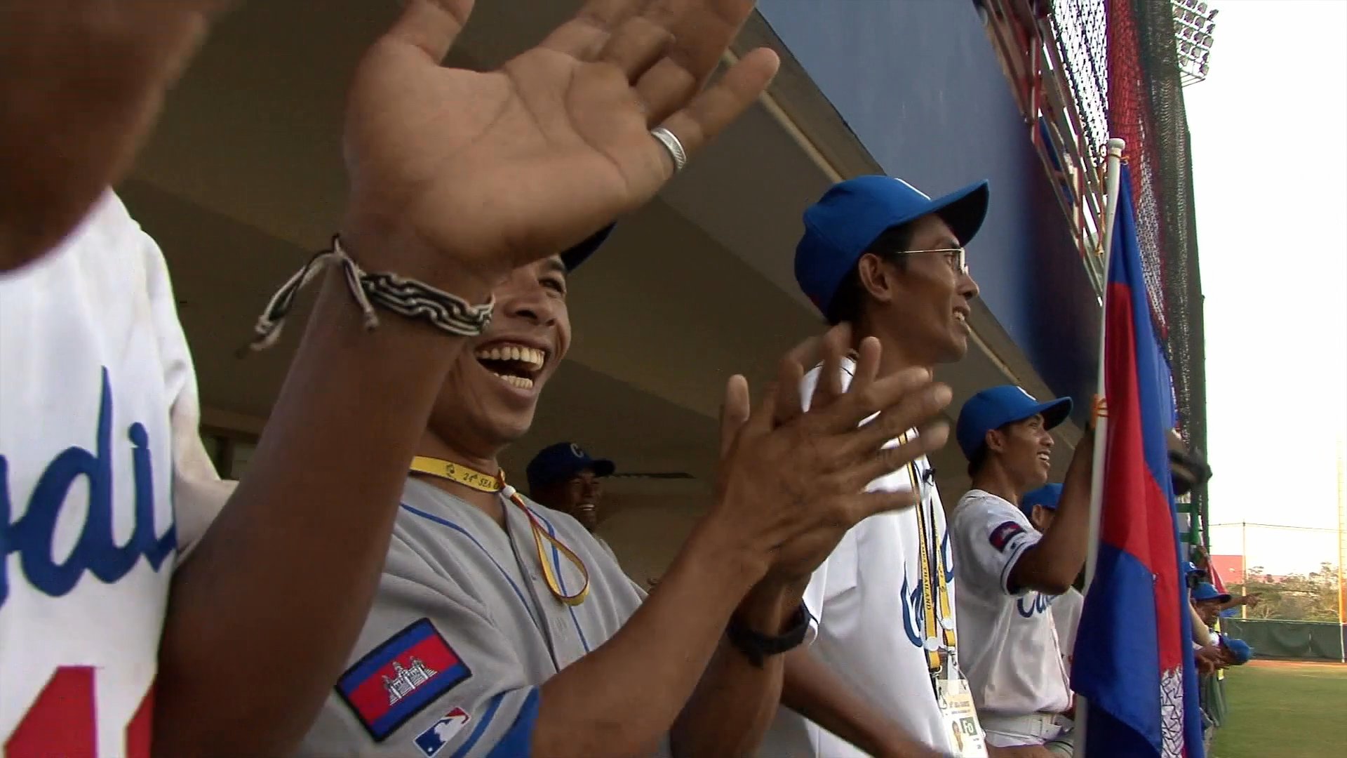 Athletes compete in a competitive baseball game between Cambodia and Malaysia at a stadium. Players execute batting and running sequences while the dugout celebrates the action.