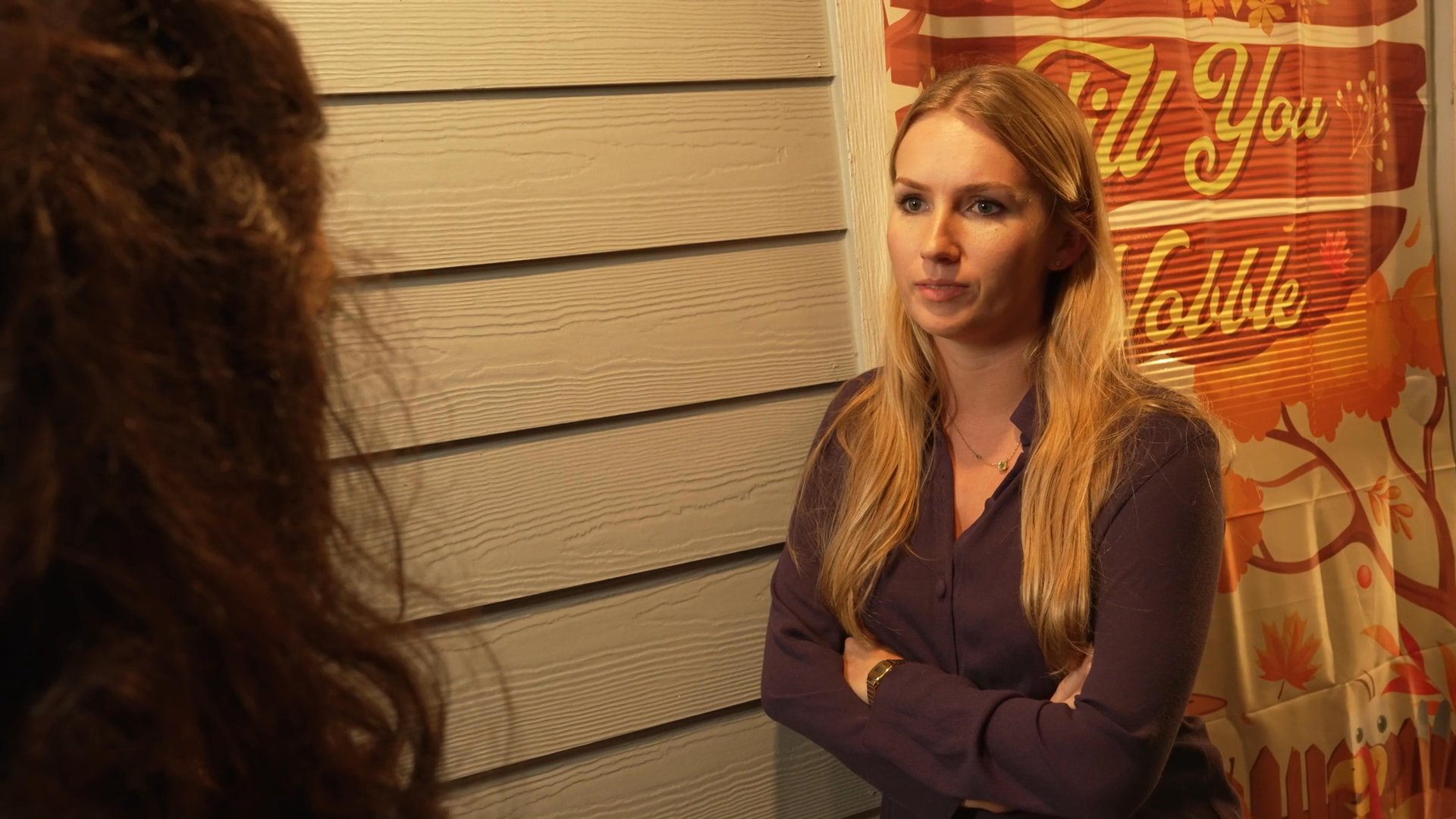 Two women engage in a deliberate conversation while standing outdoors at night. The exchange appears focused and attentive as they address each other in a dimly lit, casual setting.