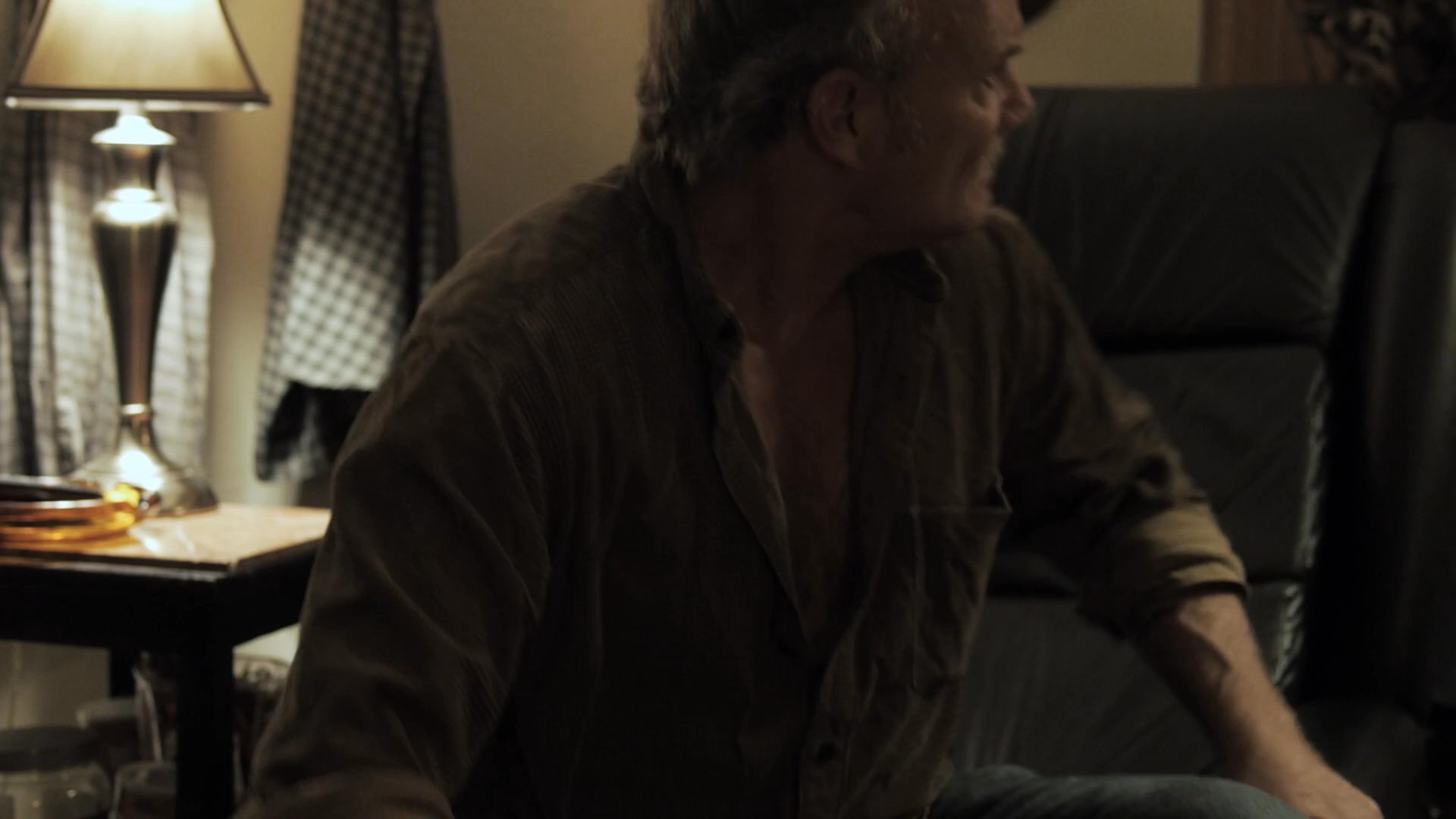 A woman observes a man who sits in deep contemplation before abruptly rising from his chair and exiting the house into the night. The scene captures a quiet, emotionally charged moment of resolution through separation.