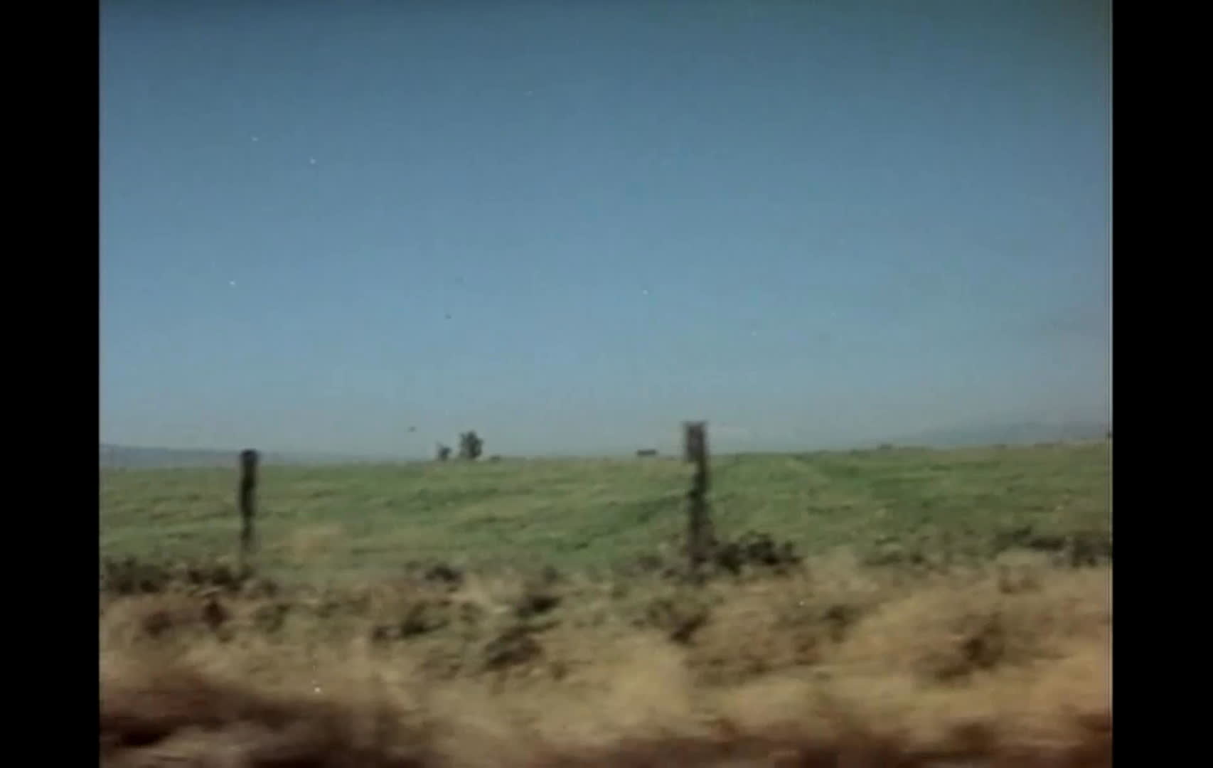 A light-blue ranch truck sits beside a weathered wooden cattle chute, followed by wide views of fenced grassland and dry, open range. The expansive landscape underscores a rancher’s wish to preserve the open, unfenced range.