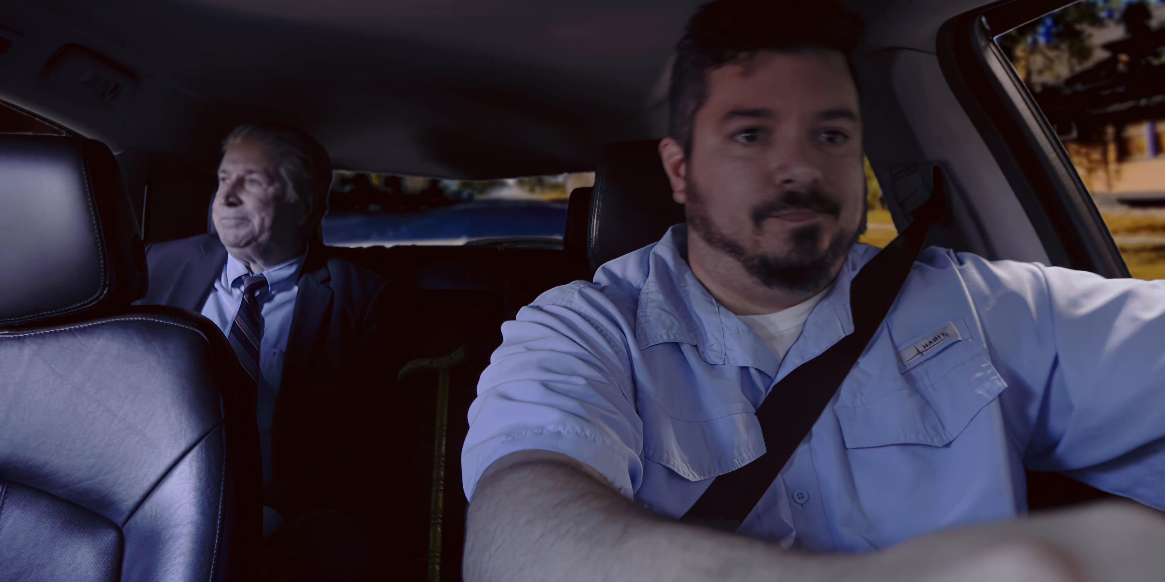 A man drives a passenger in a vehicle while they engage in conversation during their commute.