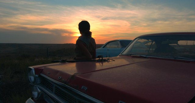 A woman leaning against a car at sunset