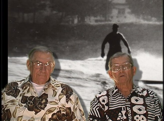 Two senior men discuss personal history and memories while archival black-and-white clips play in the background. The interview transitions into a focused conversation illustrated by historical photography.