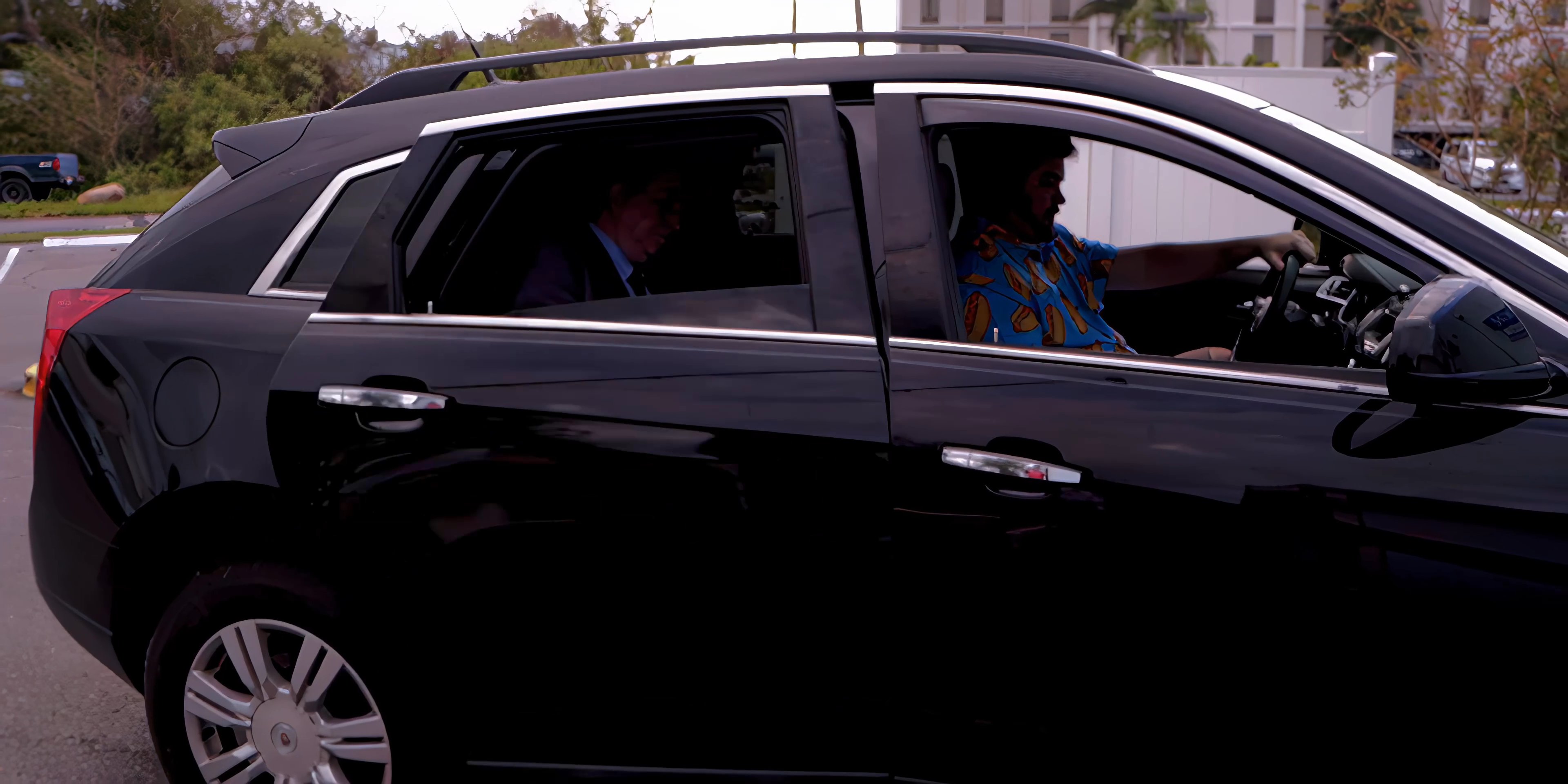 A man in a business suit enters a black car and takes a seat in the back, while the driver waits in the front seat.