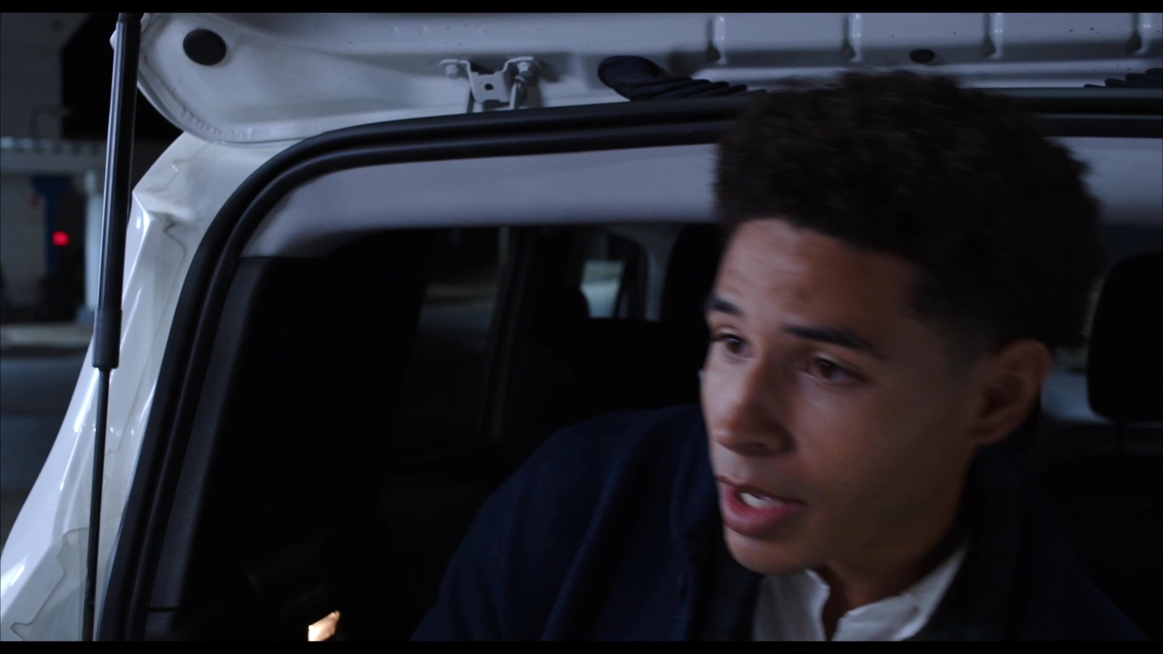 Two young men engage in an earnest conversation while standing at a gas station during the night.