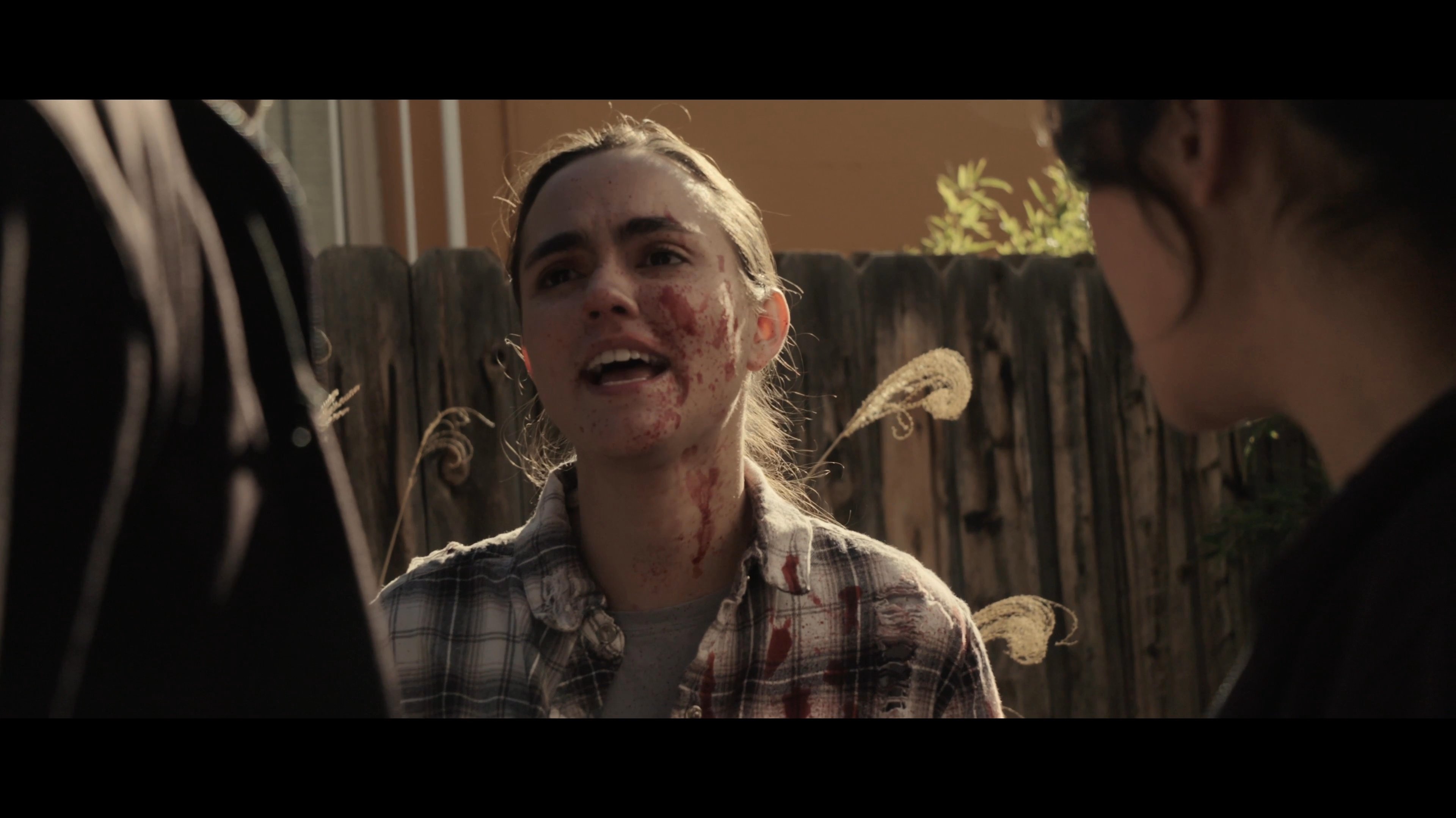 An injured woman in a plaid shirt confronts two individuals in a tense outdoor exchange. The dialogue escalates as the group navigates high-stakes interpersonal conflict.