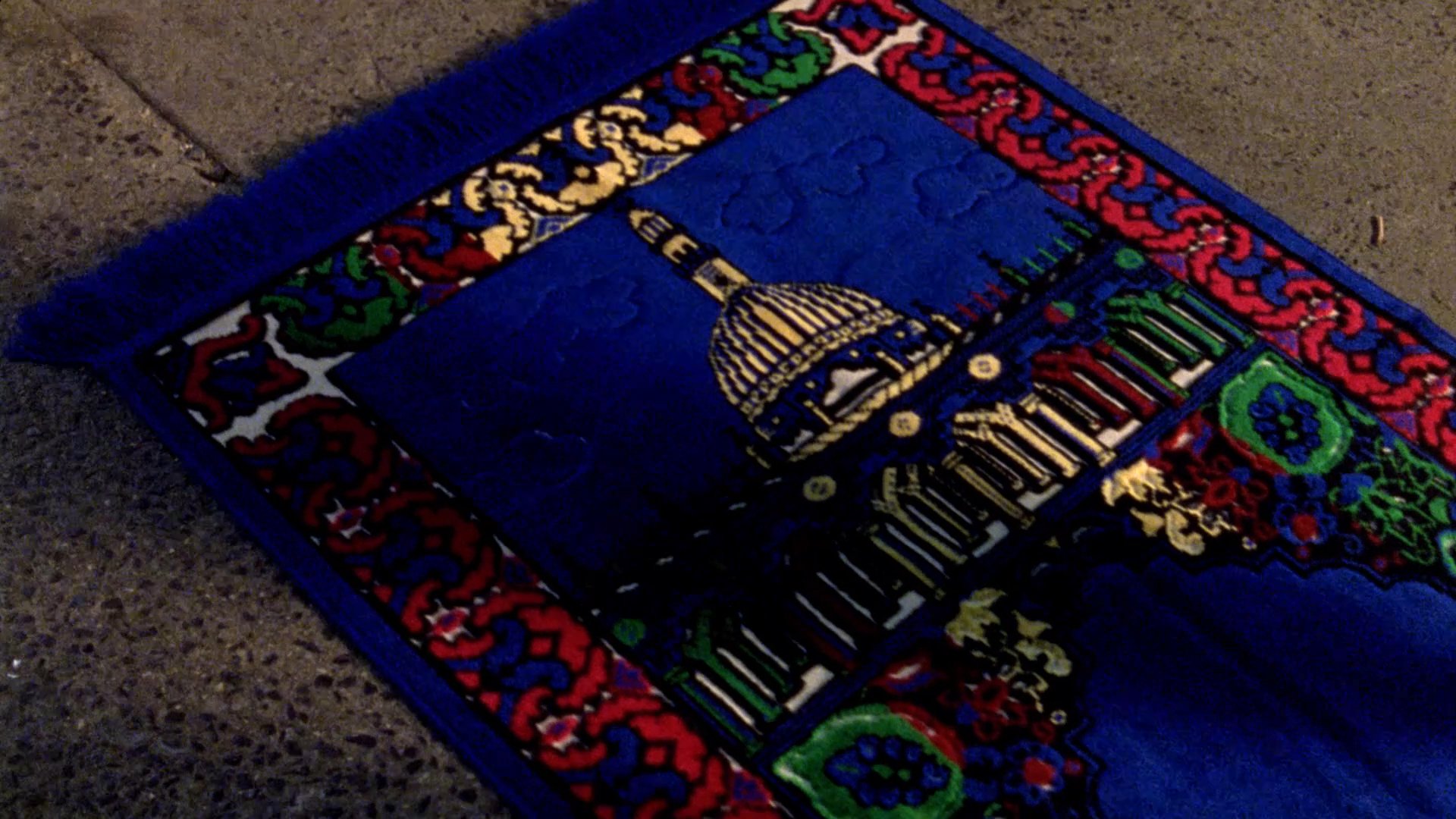 An older man wearing a traditional skullcap engages in a quiet conversation with a younger man, interspersed with shots of a prayer rug and a residential building. The sequence emphasizes cultural heritage and interpersonal connection.