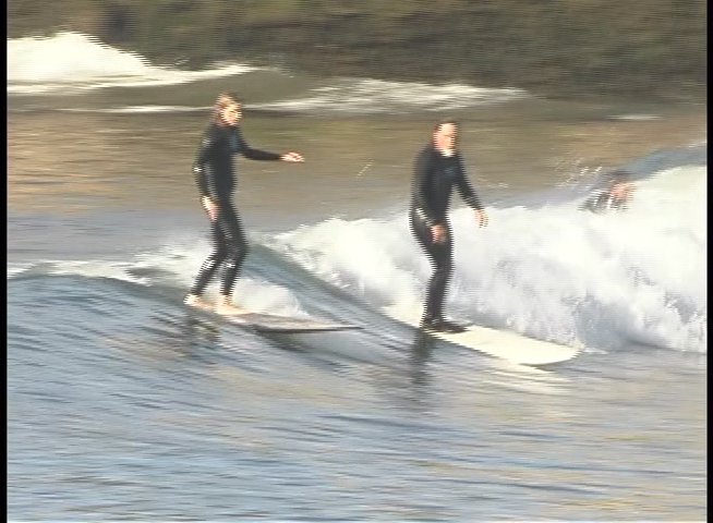 Individuals in wetsuits navigate waves on surfboards in a coastal environment, transitioning between solo and tandem surfing maneuvers.