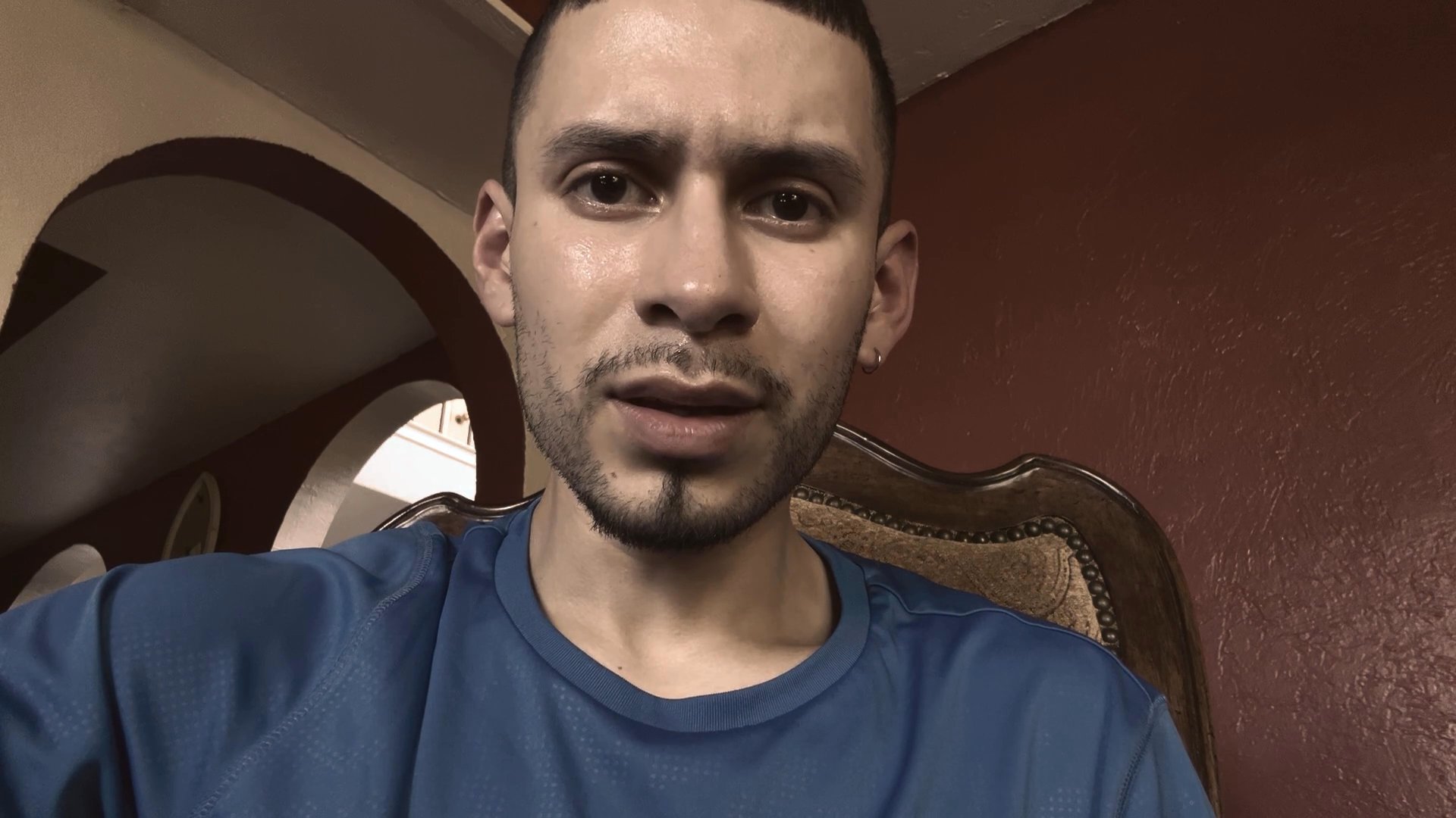 A man speaks directly to the camera, maintaining consistent eye contact while delivering a verbal message in an indoor setting.