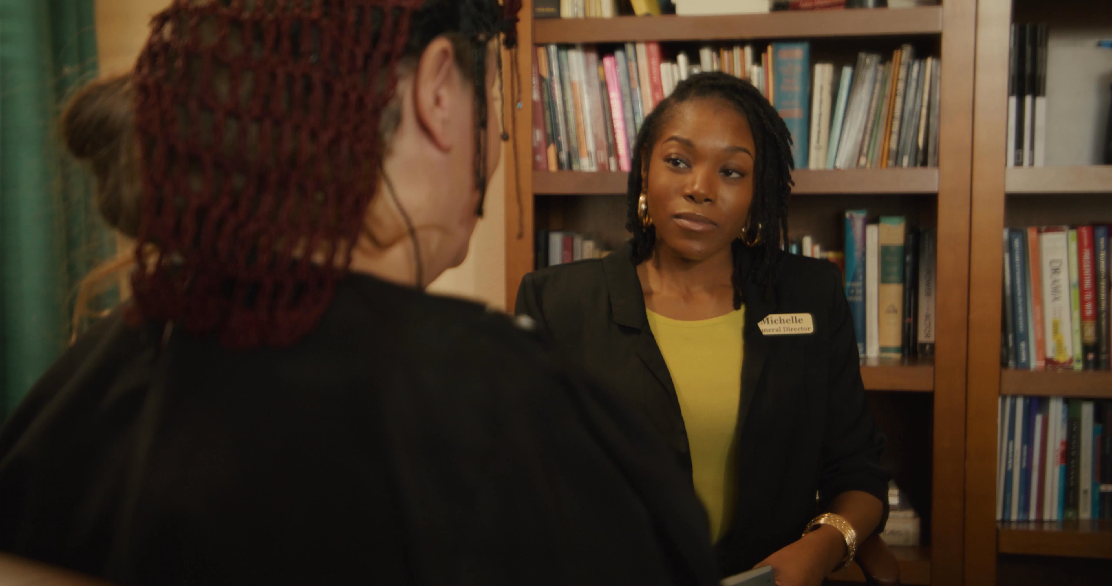 Two individuals engage in a professional, private conversation within an office setting, discussing documents and materials.