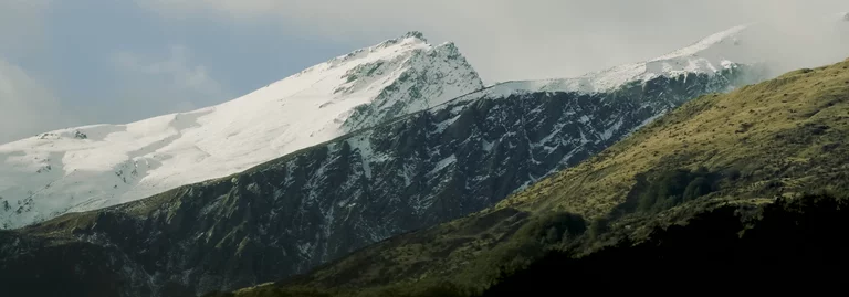 Timelapse of clouds passing through green mountains in foreground and snowy mountains in background