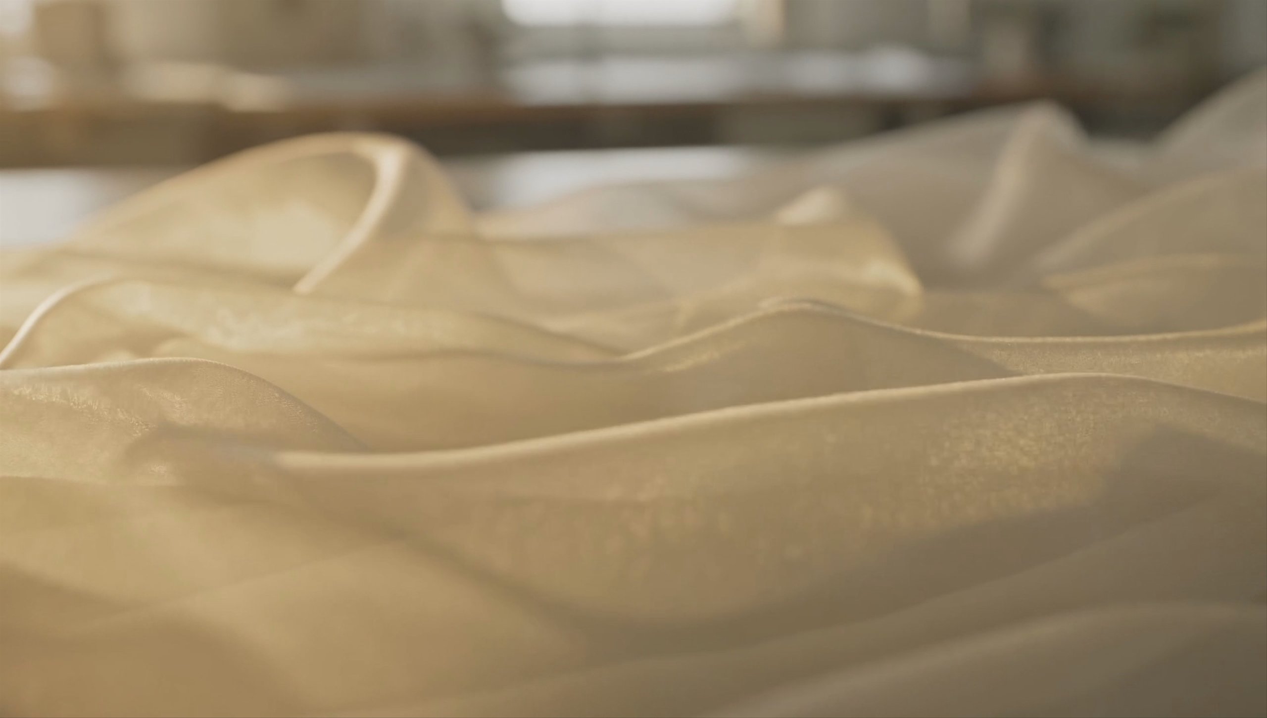 Ivory silk organza ripples in golden afternoon light inside a sunlit atelier.