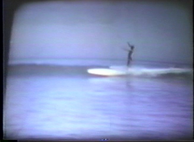 Two men recount their personal history with surfing while vintage footage of a lone surfer riding waves plays in the background.