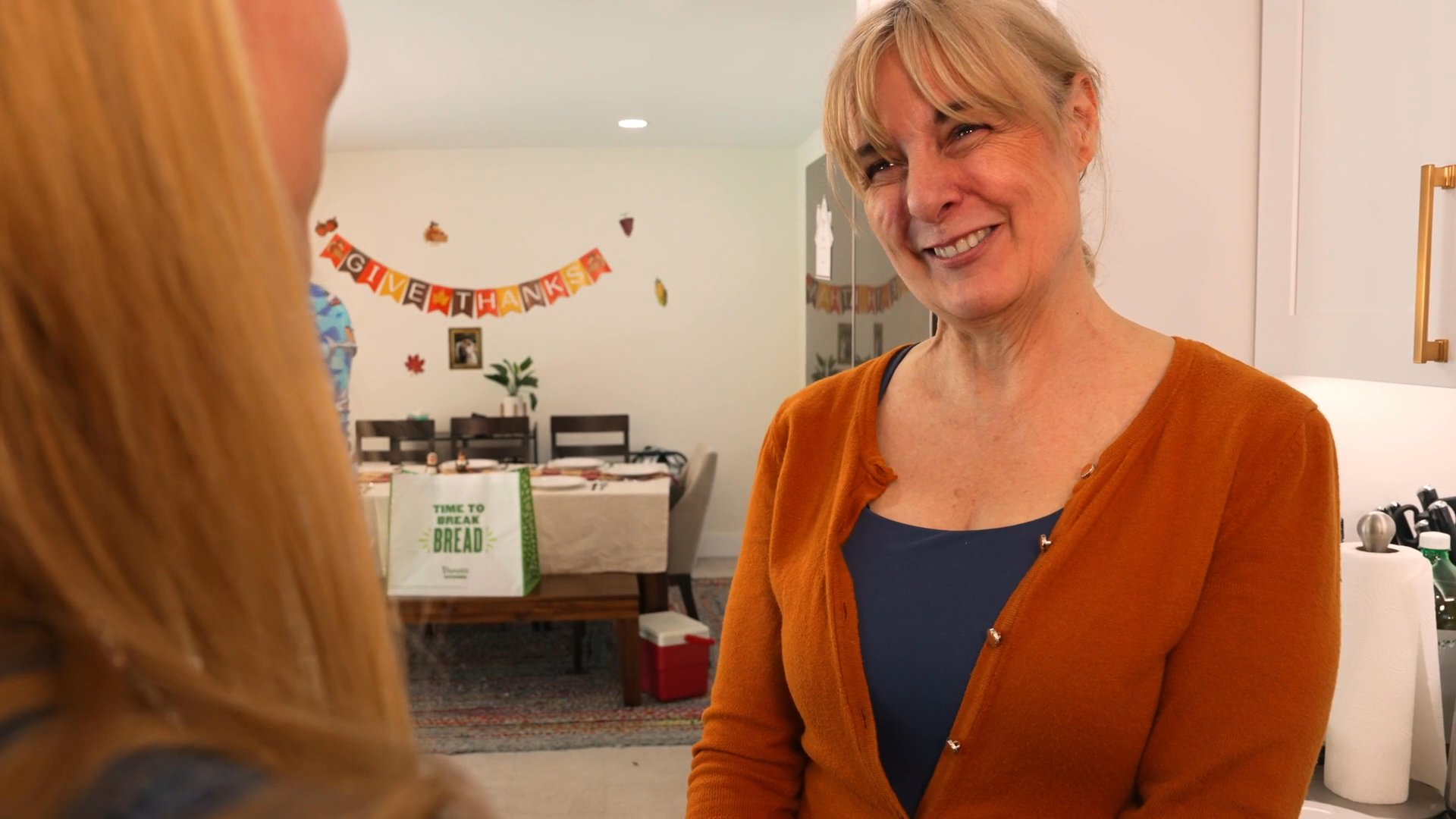 Two women share an emotional reunion with a warm embrace in a home kitchen. The scene conveys a sense of intimacy and connection between the individuals.