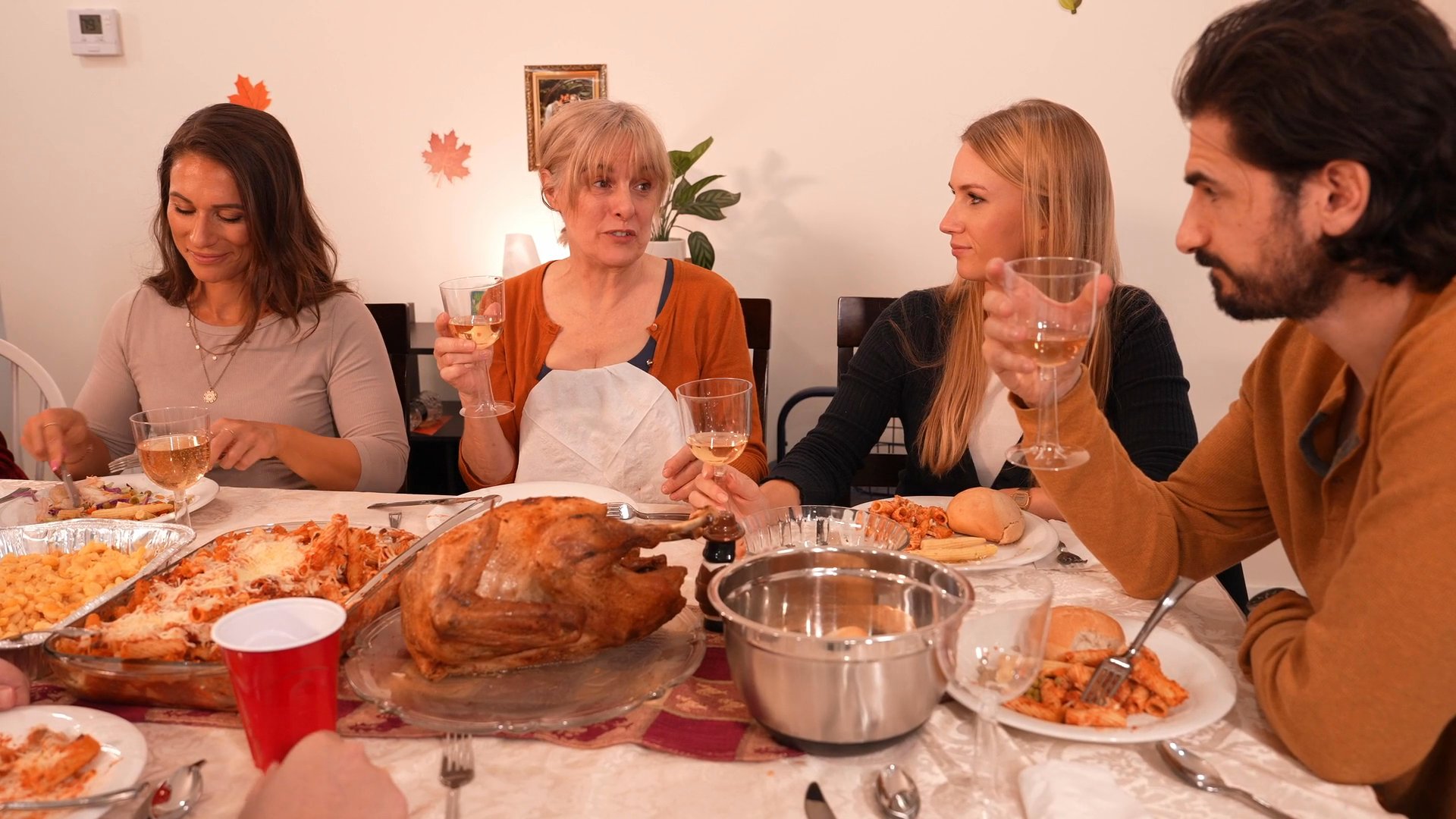 A group of adults participates in a festive holiday dinner, sharing a meal and conversation around a table set with a roast turkey and various side dishes.