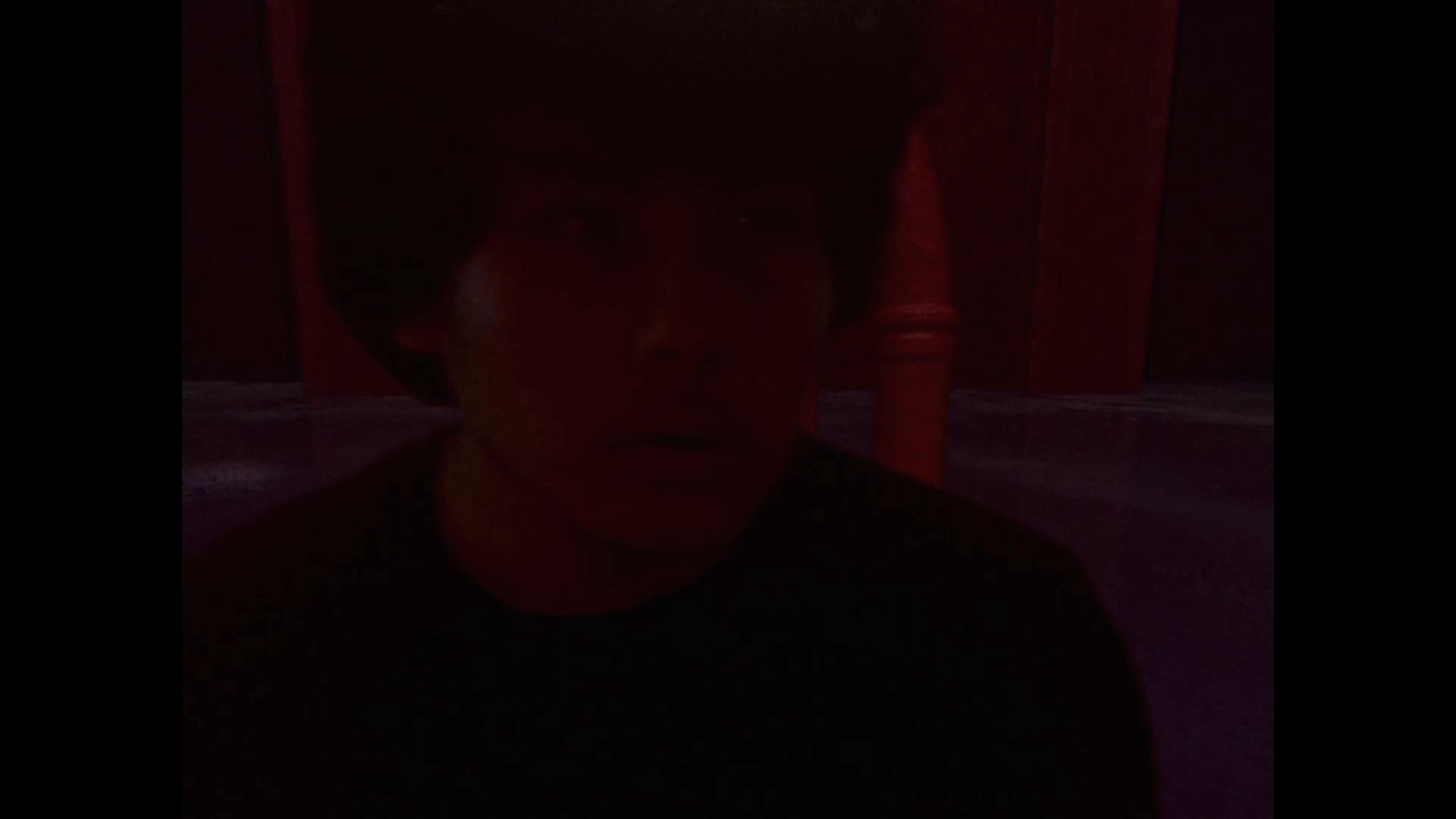 A man observes a vast, dark chamber featuring rows of architectural arches submerged in still, red-tinted water. The scene transitions from wide spatial views of the flooded interior to a close-up of the individual before fading into shadow.