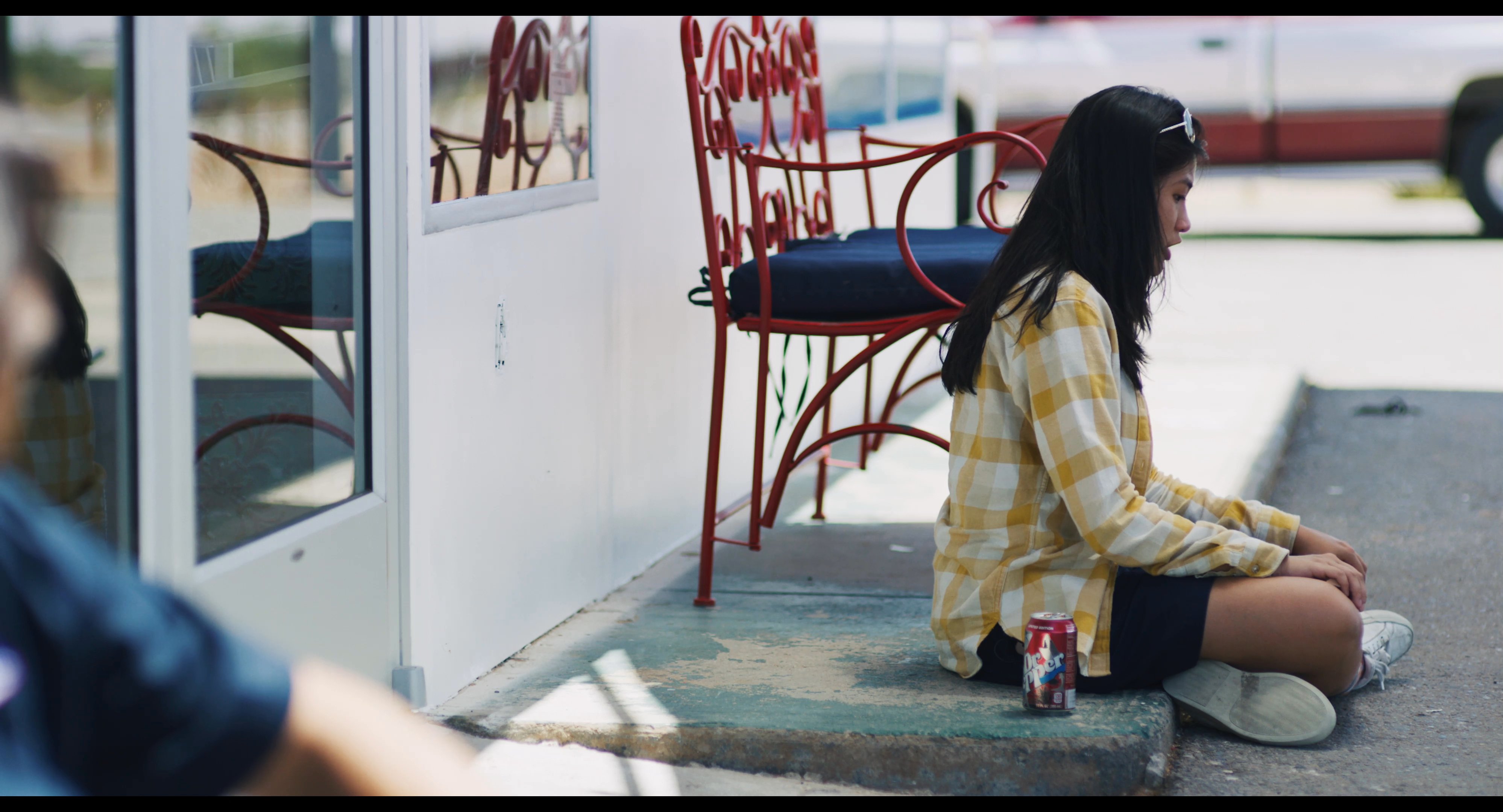 A man and a woman sit on the pavement outside a glass-fronted building, taking a quiet break during their travels.