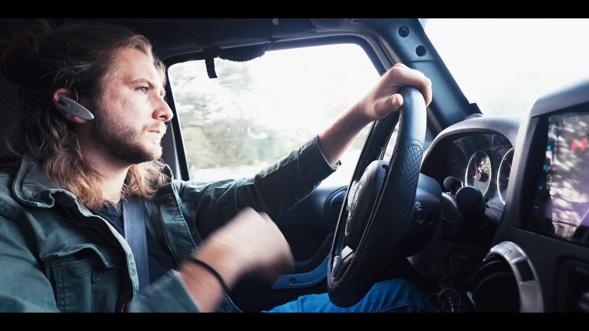 A man drives a vehicle while engaging in an active phone conversation with another person who is relaxing on a sofa. The scene alternates between the driver's perspective and the individual on the phone to illustrate ongoing remote coordination.