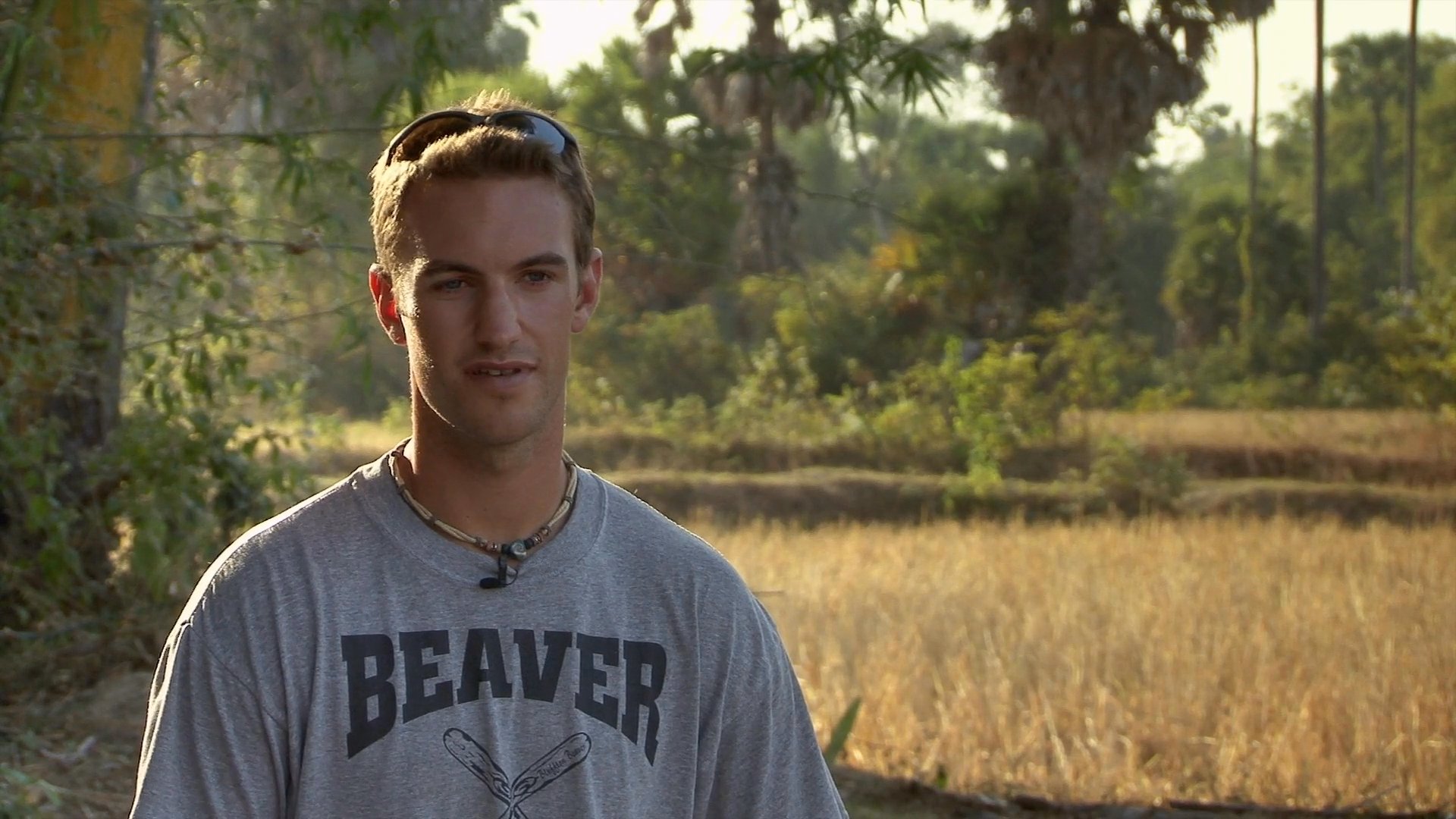 Two men speak directly to the camera while positioned in a sunlit, rural landscape. They engage in a candid conversation, alternating as they share perspectives.