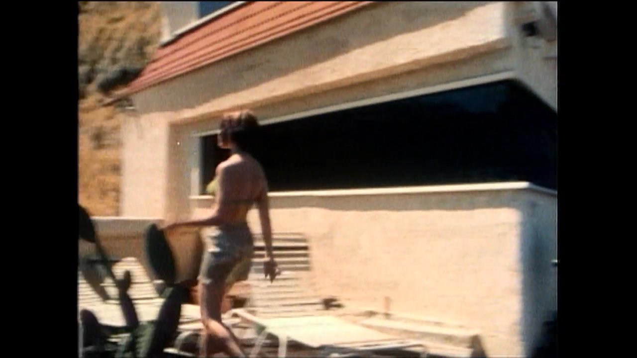 A woman sunbathing on a terrace engages in a tense conversation with a man, leading to a heated interpersonal exchange in a residential backyard setting.