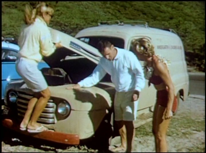 A group of surfers transitioning from the beach experience engine difficulties with their vintage van. The individuals attempt to inspect and troubleshoot the vehicle alongside a coastal road.