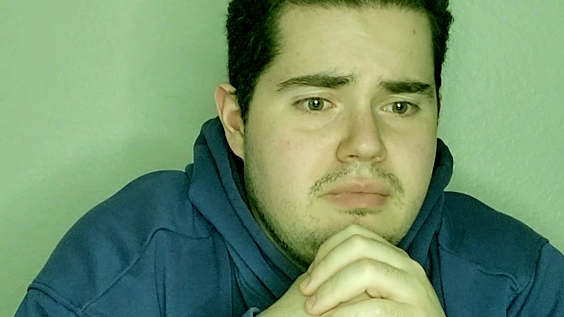 A young man with dark hair and a blue hoodie delivers a focused commentary, exhibiting varied facial expressions while speaking to the camera.