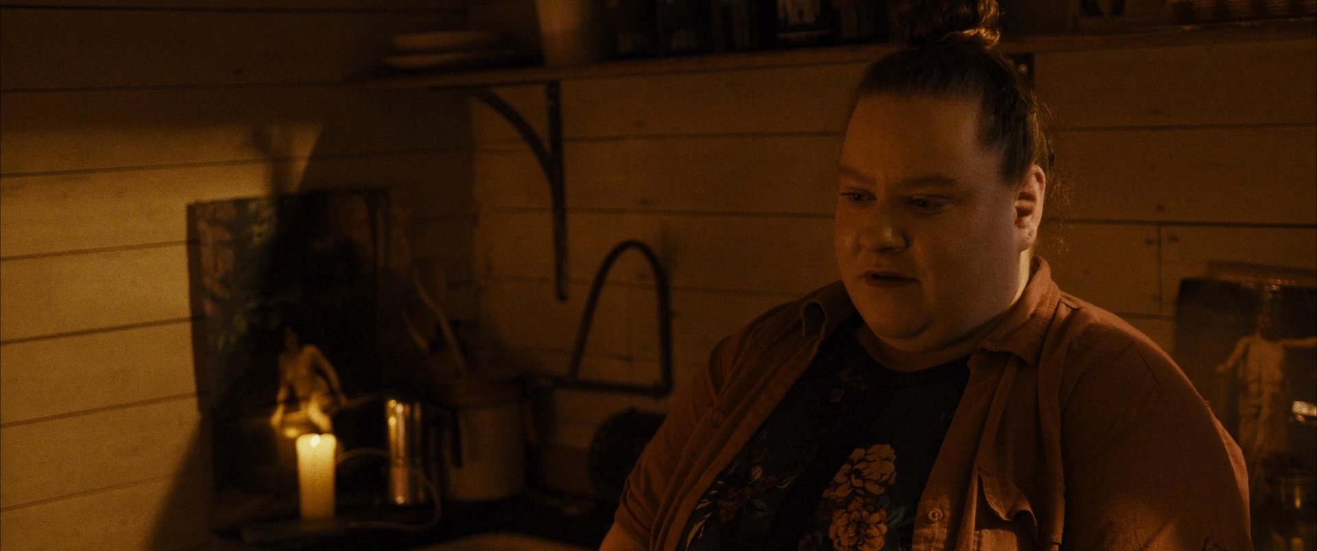 Two individuals engage in a serious discussion inside a dimly lit cabin, illuminated primarily by a lantern and candlelight.