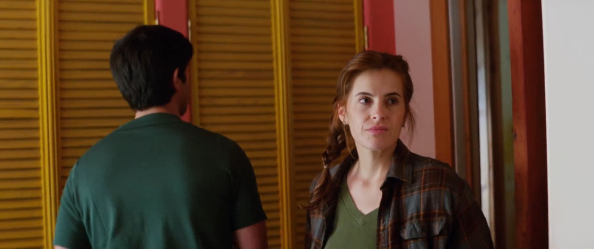 Two men engage in a tense, serious discussion inside a room while a woman observes the interaction from the background. The conversation shifts as the woman approaches and enters the frame, altering the dynamic of the encounter.