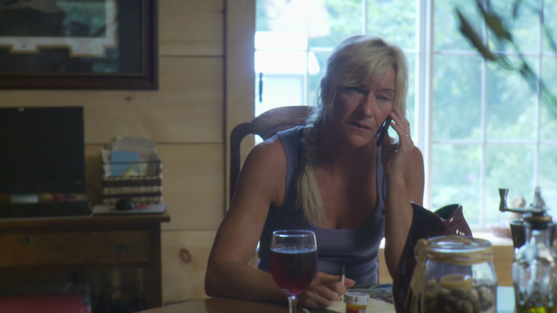 A woman sits at a table and conducts a serious conversation on her mobile phone while indoors.