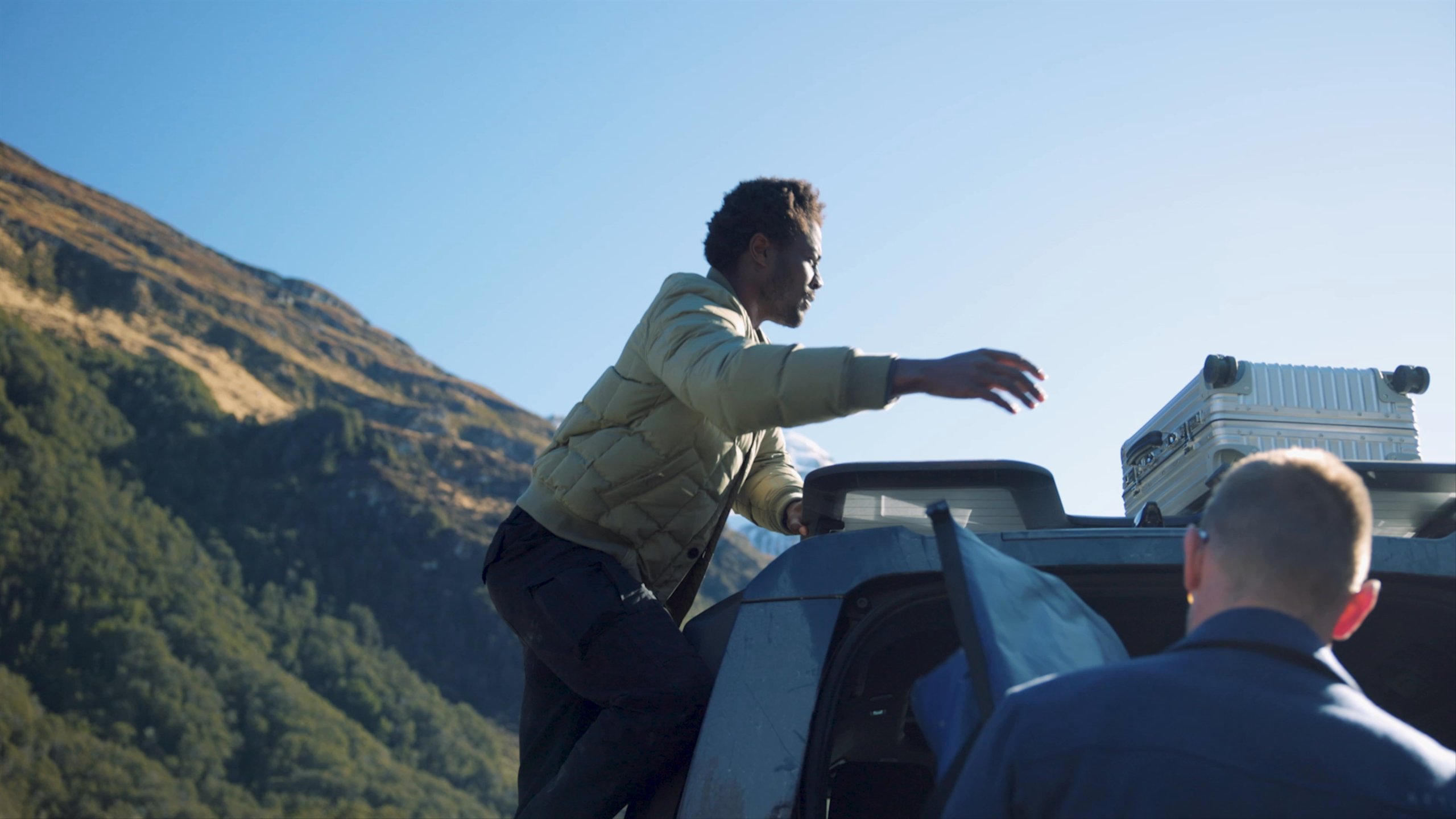 Video of man pulling luggage from the top of a Defender vehicle in New Zealand landscape