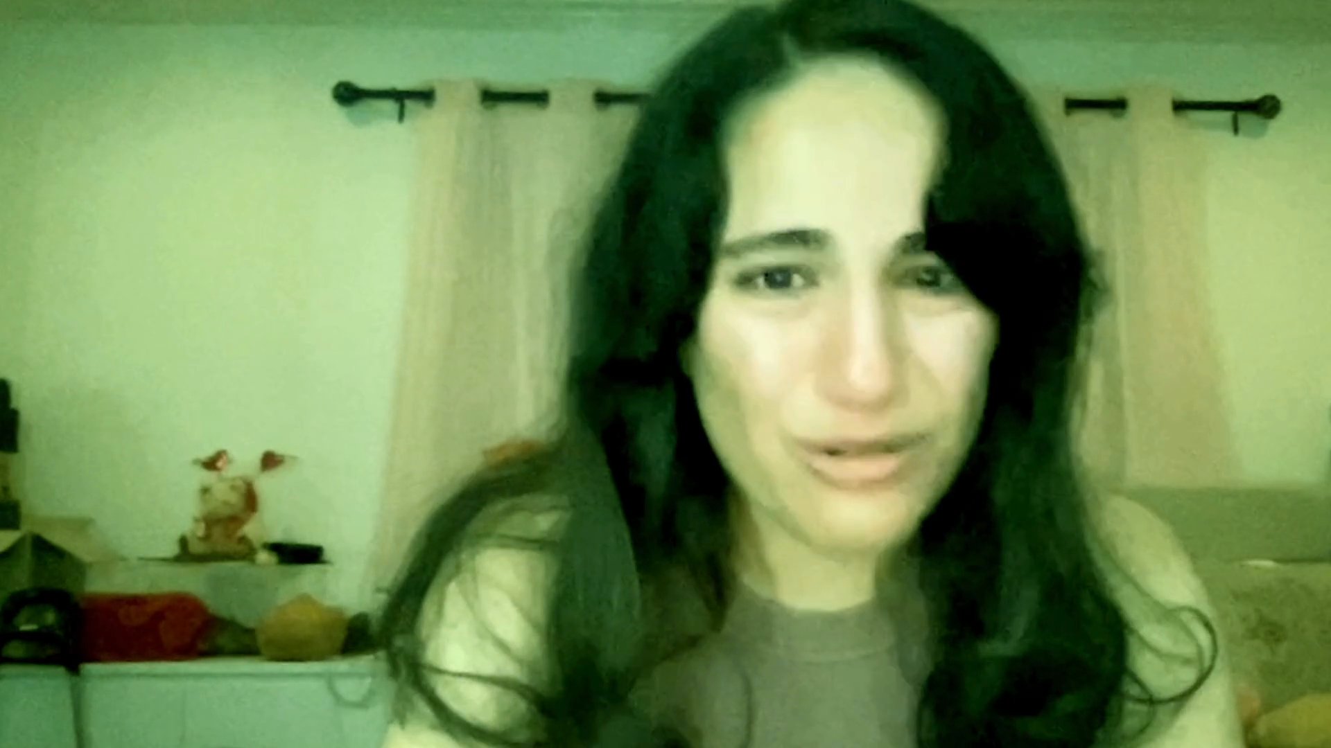 A woman exhibits visible distress and sheds tears while speaking directly into the camera in a domestic setting.