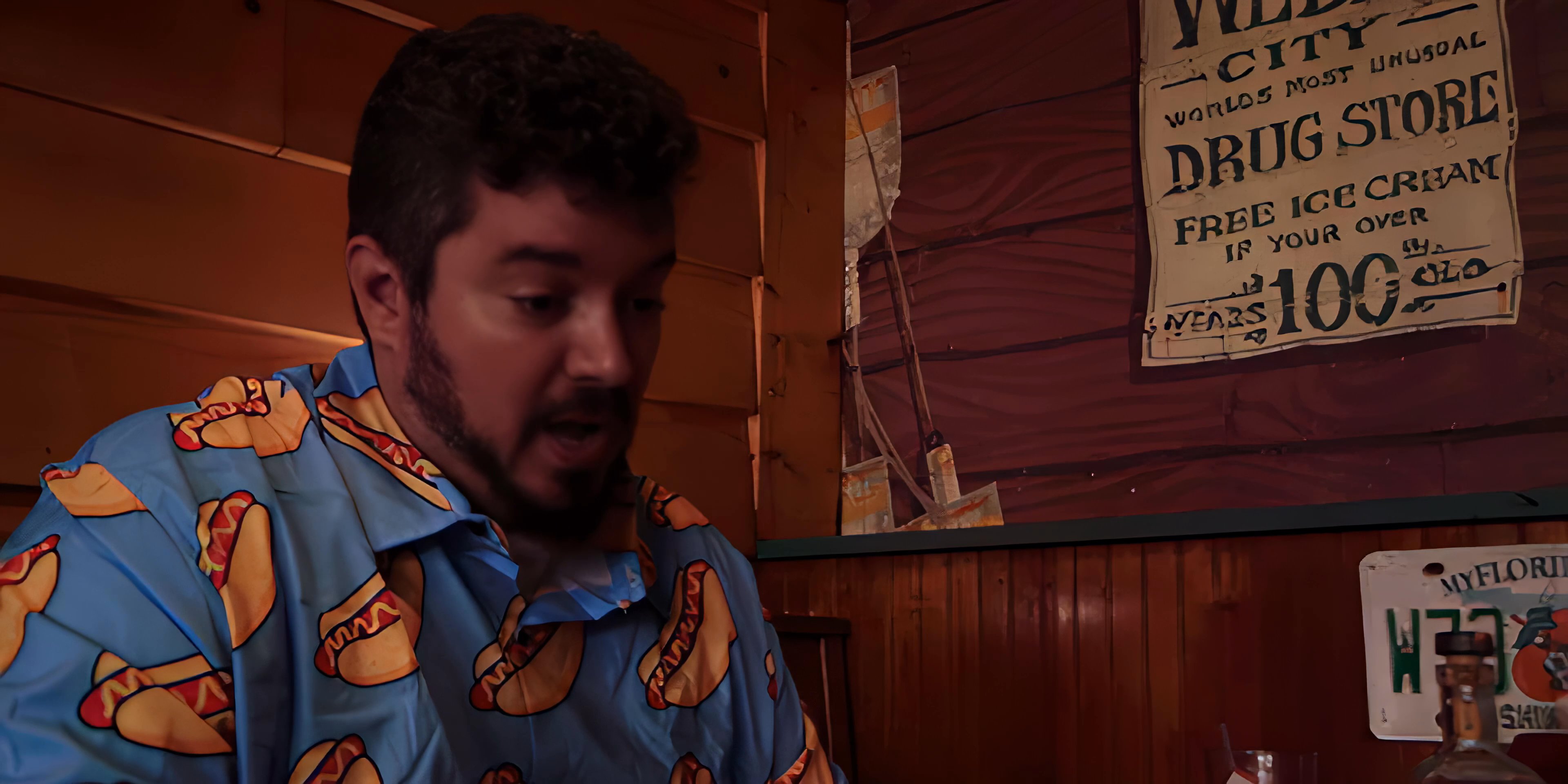 Two men engage in an informal discussion while seated at a wooden-paneled diner booth. The interaction alternates focus between the participants as they maintain a steady exchange.