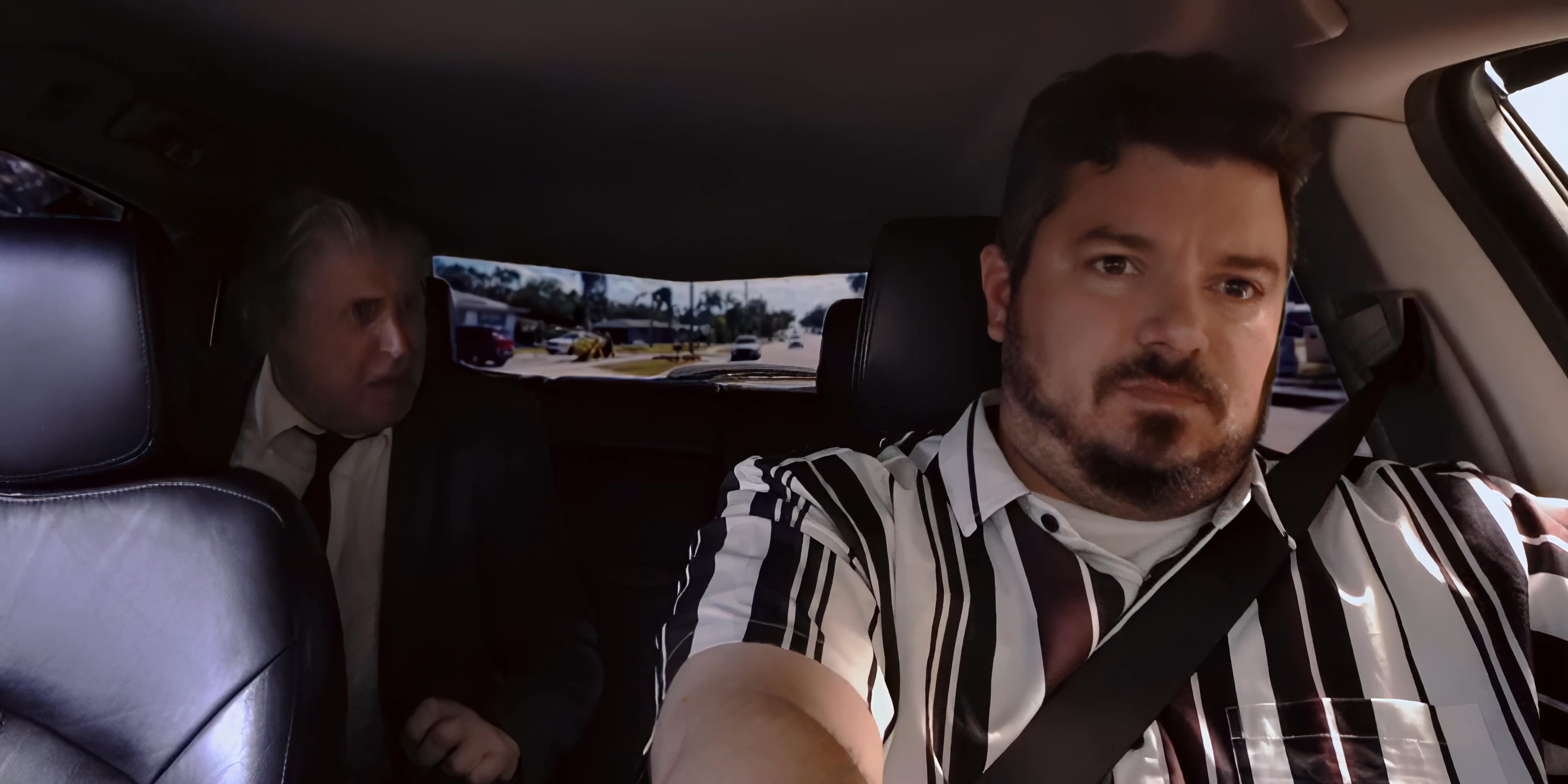 A driver and his passenger engage in a tense conversation while traveling in a car. The passenger appears visibly distressed or agitated as they look out the window during the journey.