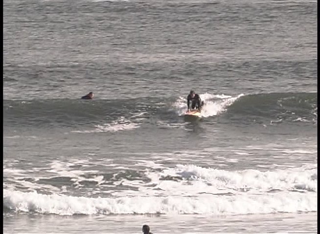 Professional surfer Michel Junod discusses his craft while on-camera, interspersed with footage of him riding ocean waves on a surfboard.