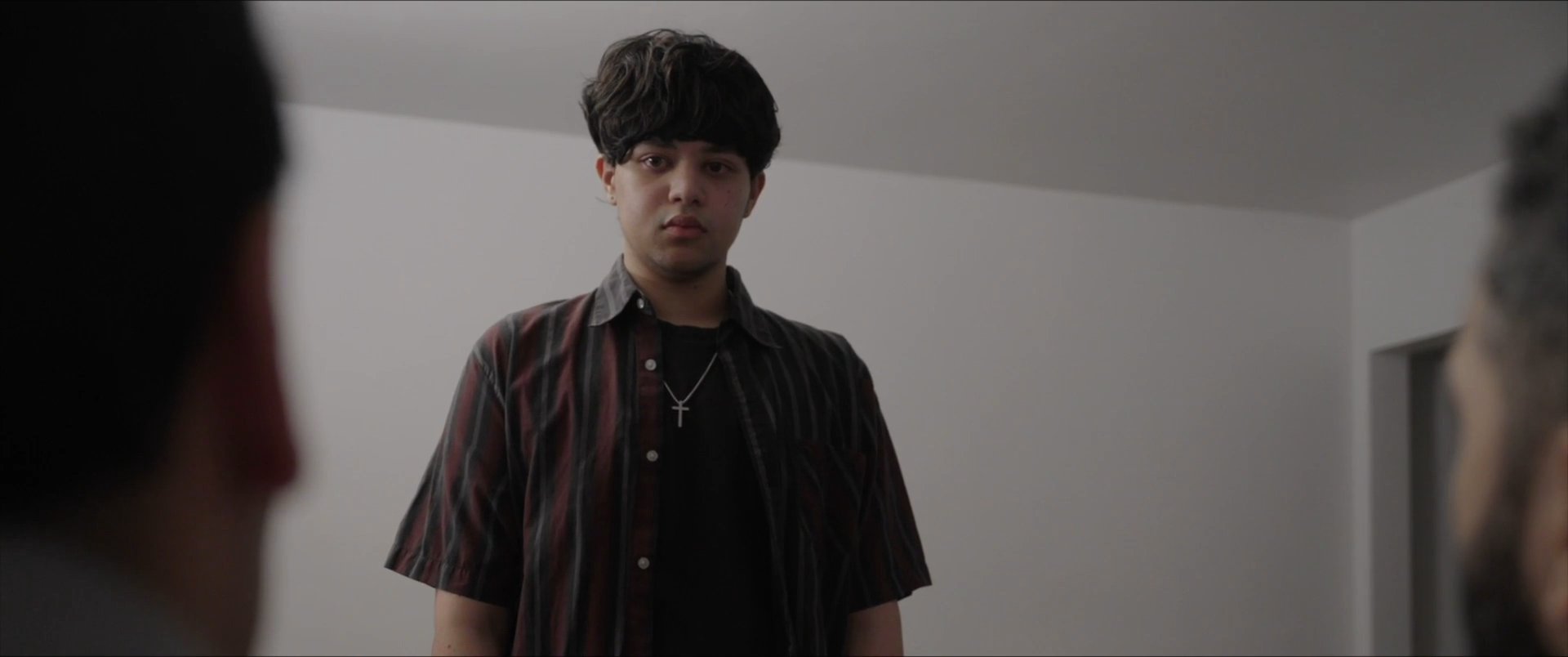 Two professionals engage in a tense discussion with a young man in a minimalist office setting. The interaction involves careful observation and verbal exchange, reflecting a serious or sensitive situation.
