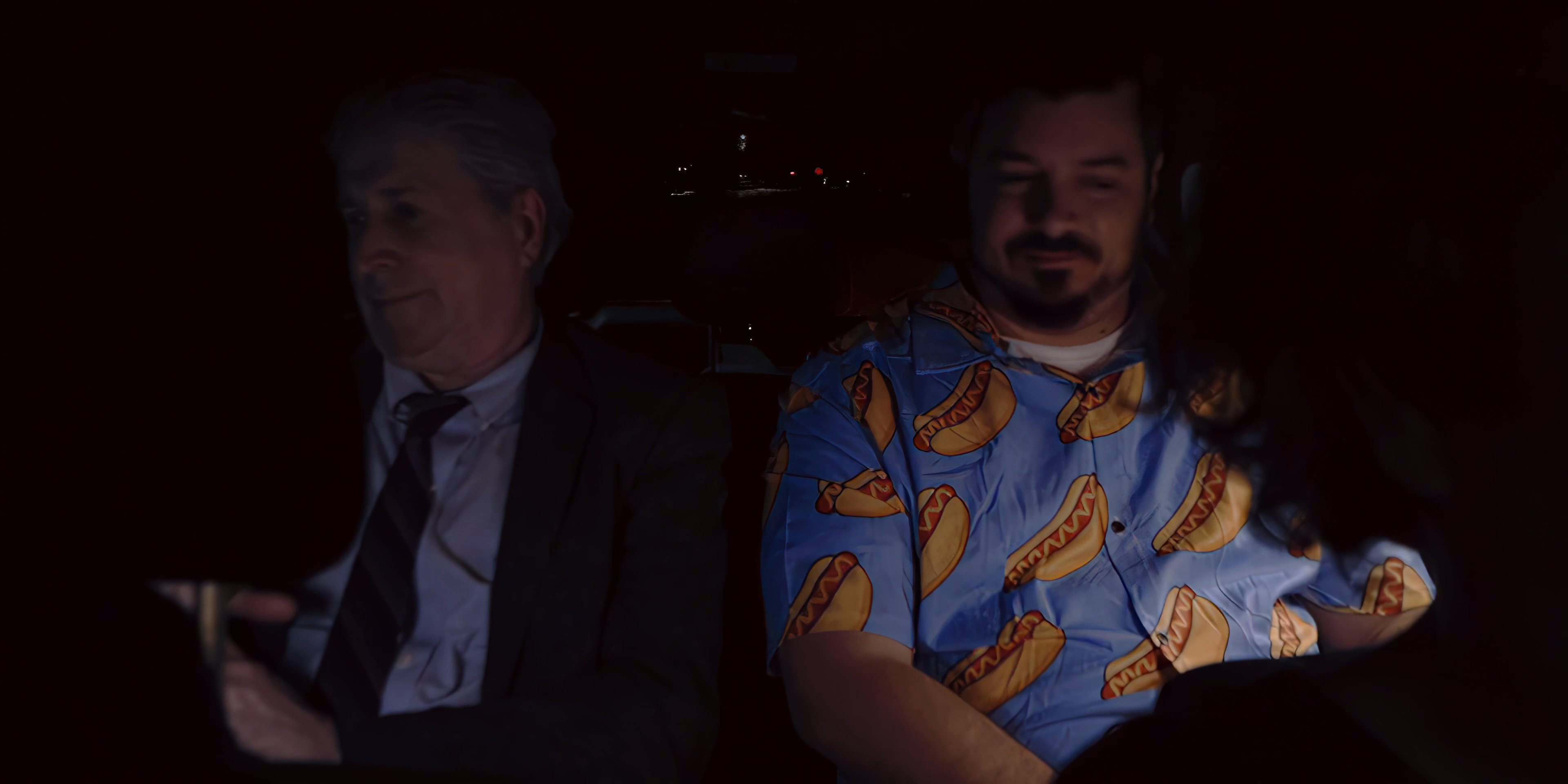 Two men engage in a serious discussion while seated together in a dimly lit vehicle.