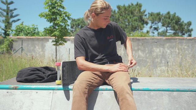 Blonde skateboarder using his smartphone while sitting on a ramp 