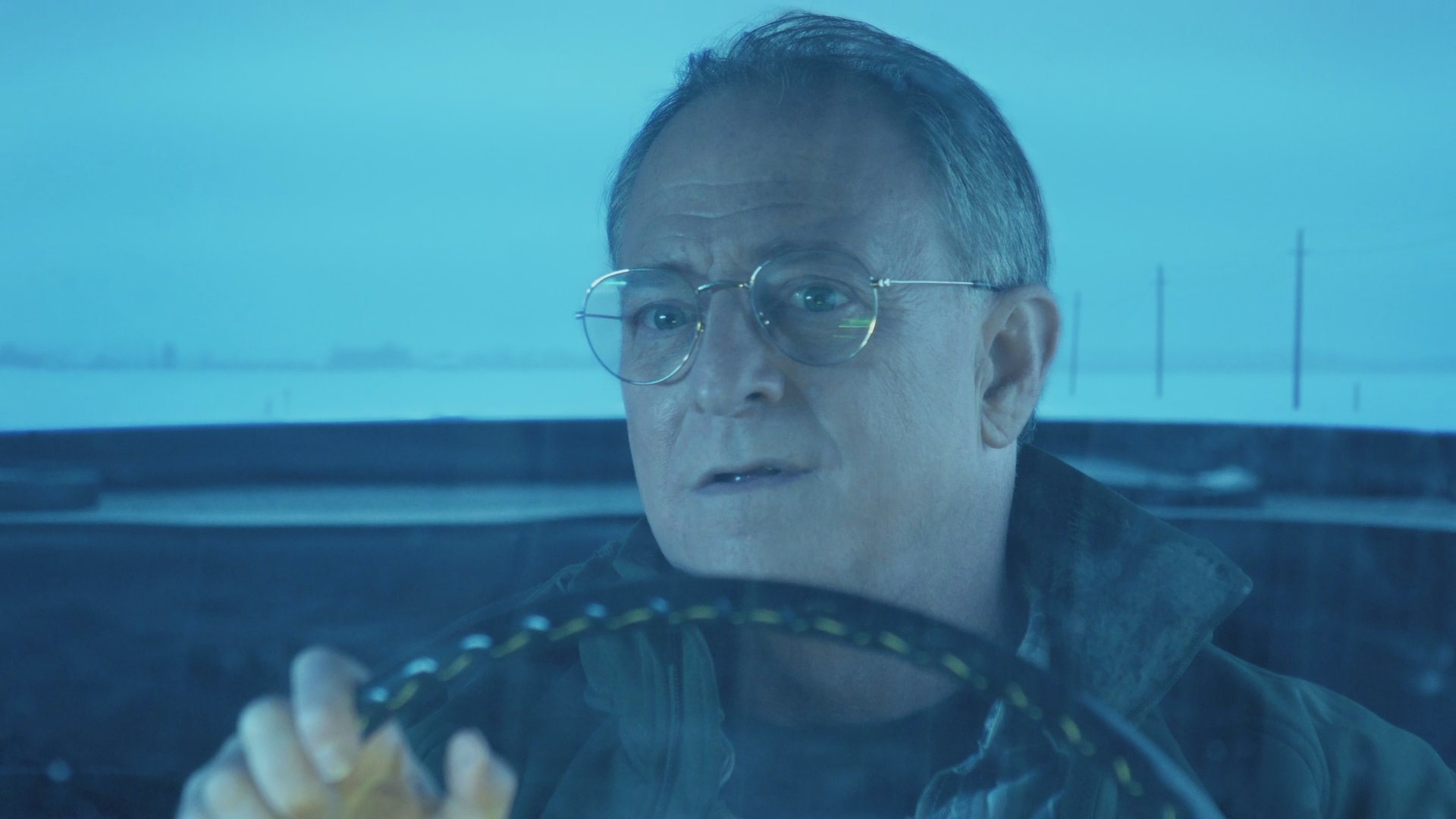 A man and woman engage in a quiet conversation while traveling together in a car through a cold, winter landscape. The scene focuses on their interaction and the serene atmosphere of their commute.