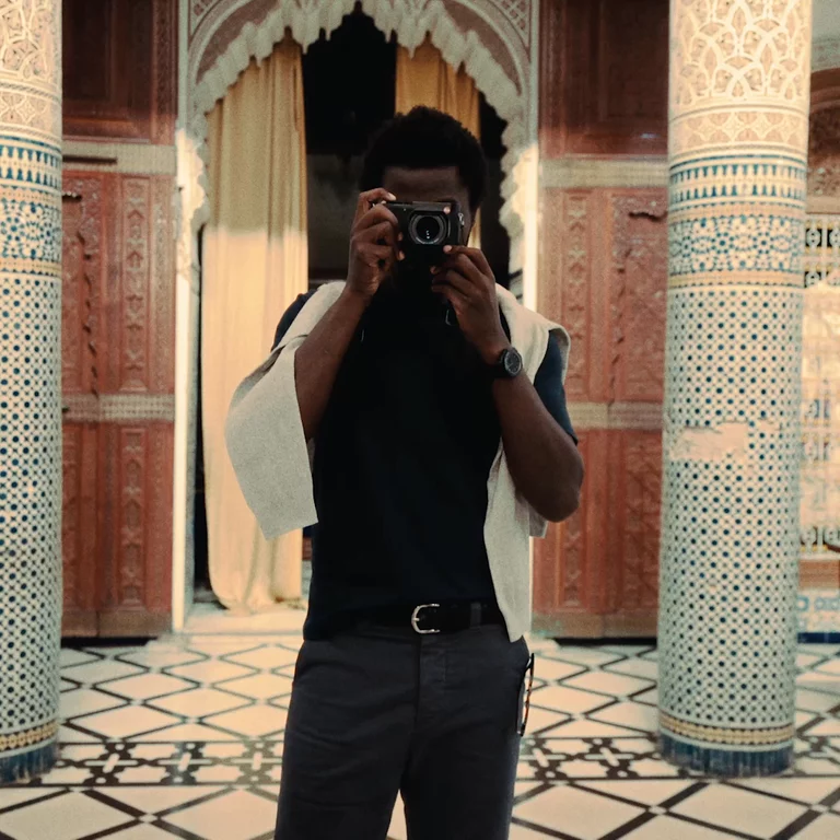 Video of man taking a portrait straight ahead with traditional Moroccan tiled architecture in the background