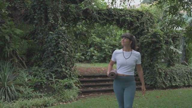 Yoga teacher walking in the park while holding a yoga mat