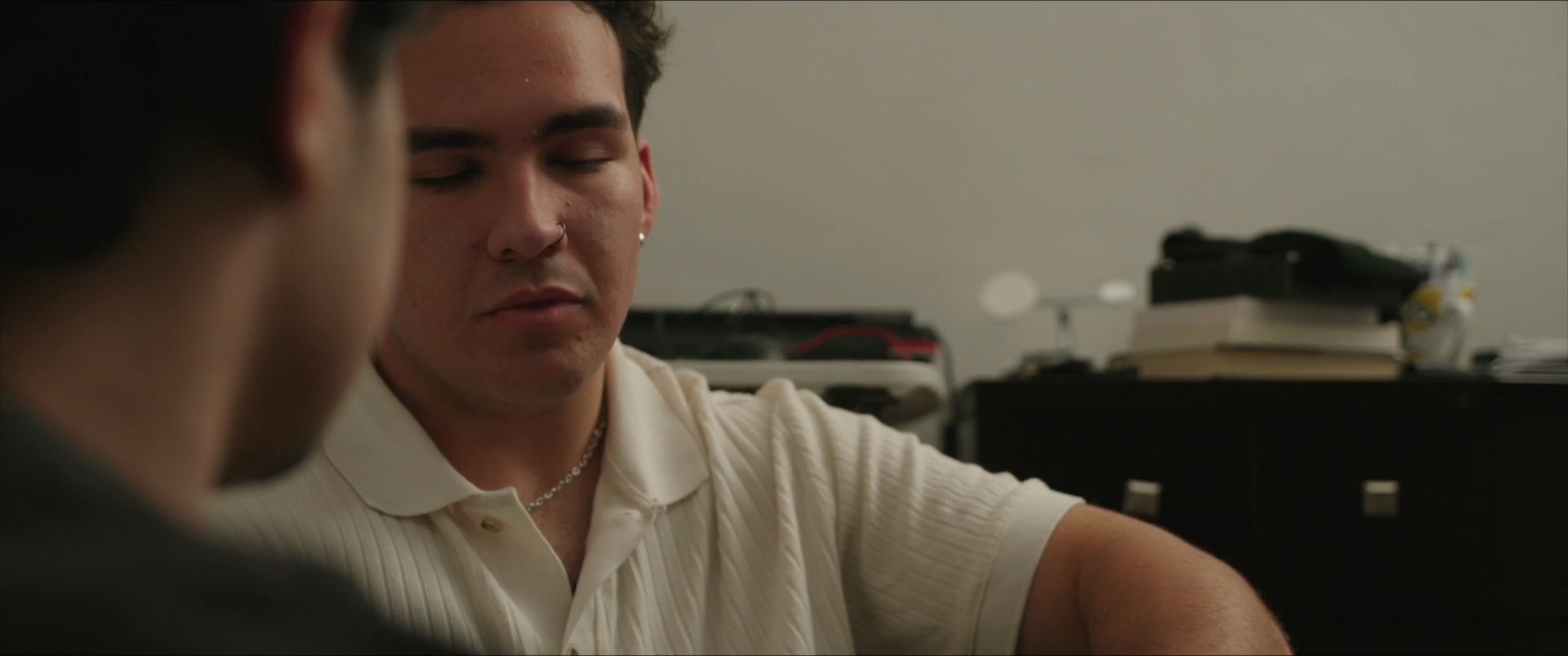 Two individuals engage in a focused, seated conversation within a dimly lit indoor environment. They alternate speaking and listening, maintaining eye contact throughout their interaction.