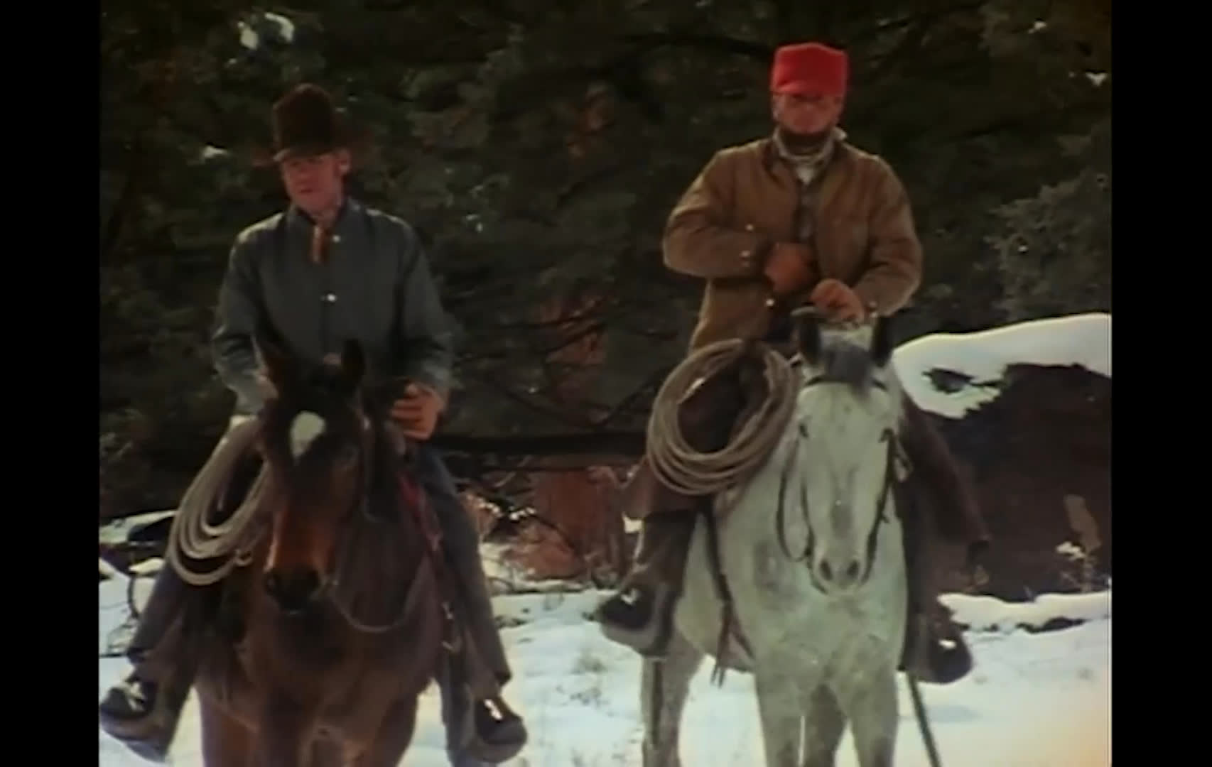 A rancher speaks reflectively as two riders travel through a snowy range and cattle gather near a farmhouse. A shadowed figure watches from beside an enclosure, while the narration raises questions about how the landscape may change in the coming years.