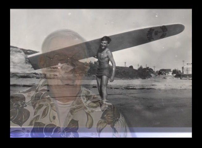 An elderly man shares personal reflections while archival imagery of himself as a young surfer on a beach is layered into the background. The visual transition highlights the continuity between his past experiences and present-day narrative.